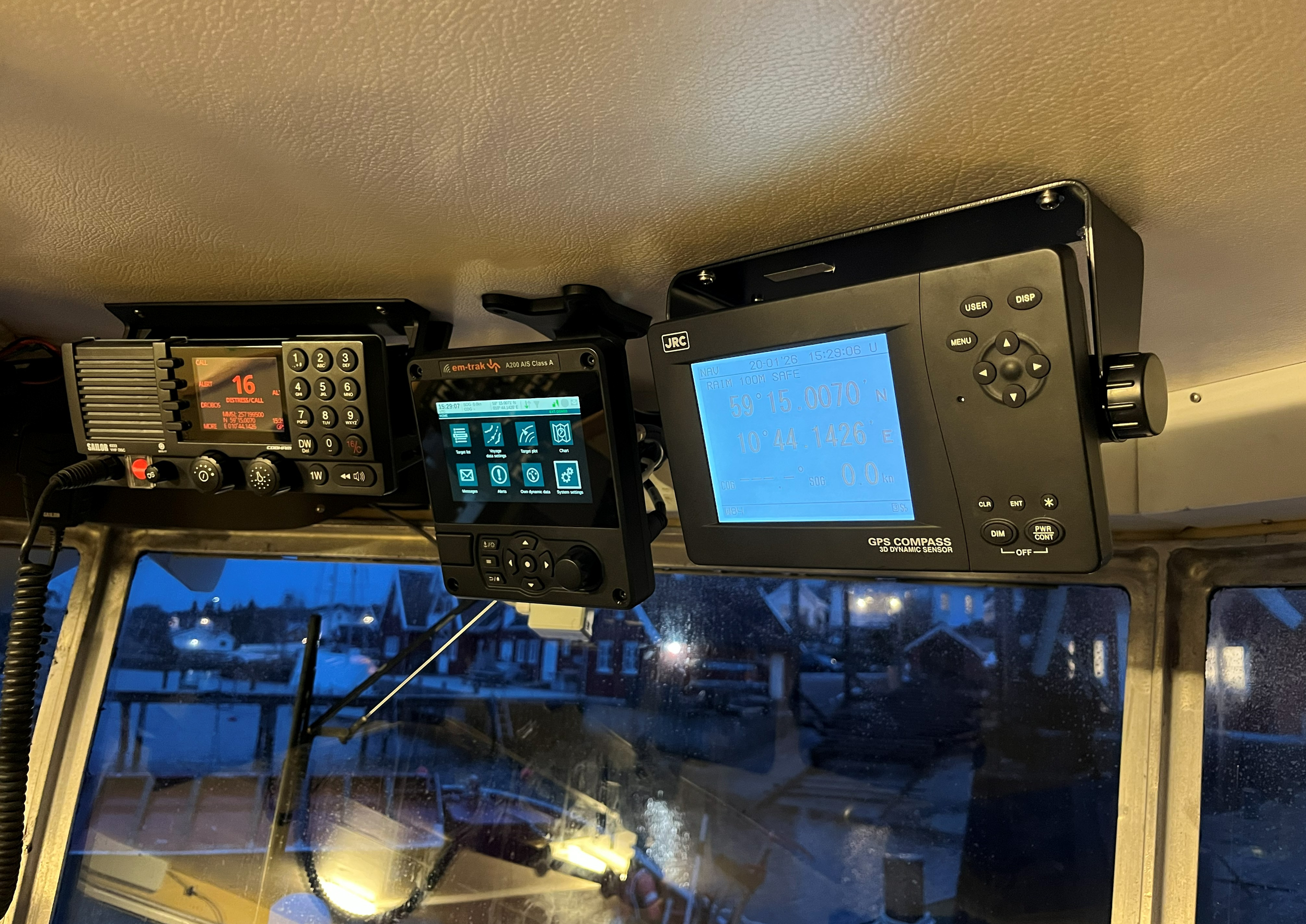 Navigasjons- og radioutstyr i styrehuset på en båt, med maritim VHF-radio, AIS-skjerm og GPS-kompass.