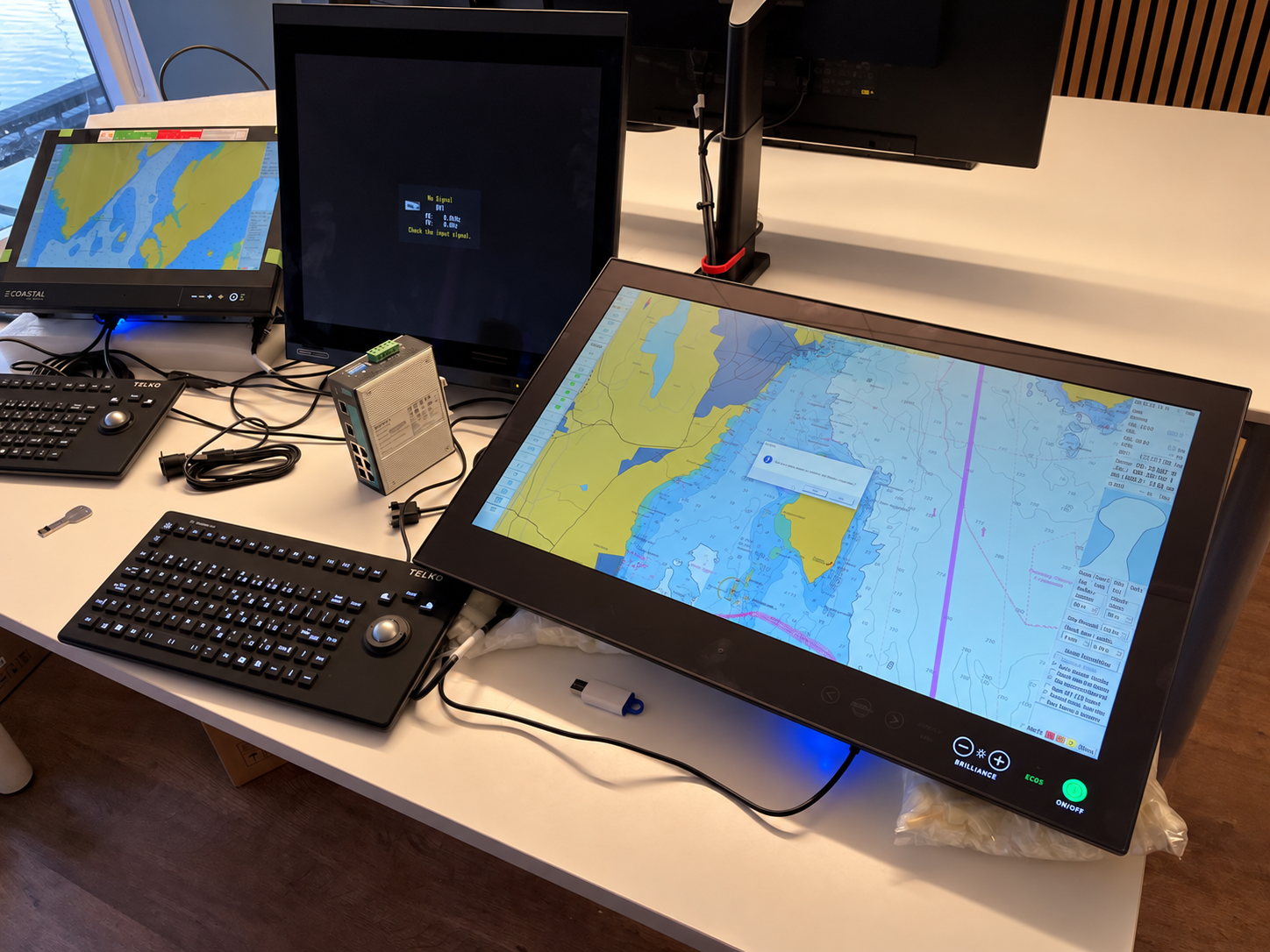 Telko TECDIS navigasjons- og kartdataskjerm på et kontrollbord med geografisk kart, tastatur, kontrollpanel, og tilkoblet utstyr.