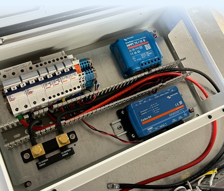 Elektrokomponenter i et kontrollskap, inkludert sikringer, ledninger, og ulike enheter, med en metallramme og en åpen topp