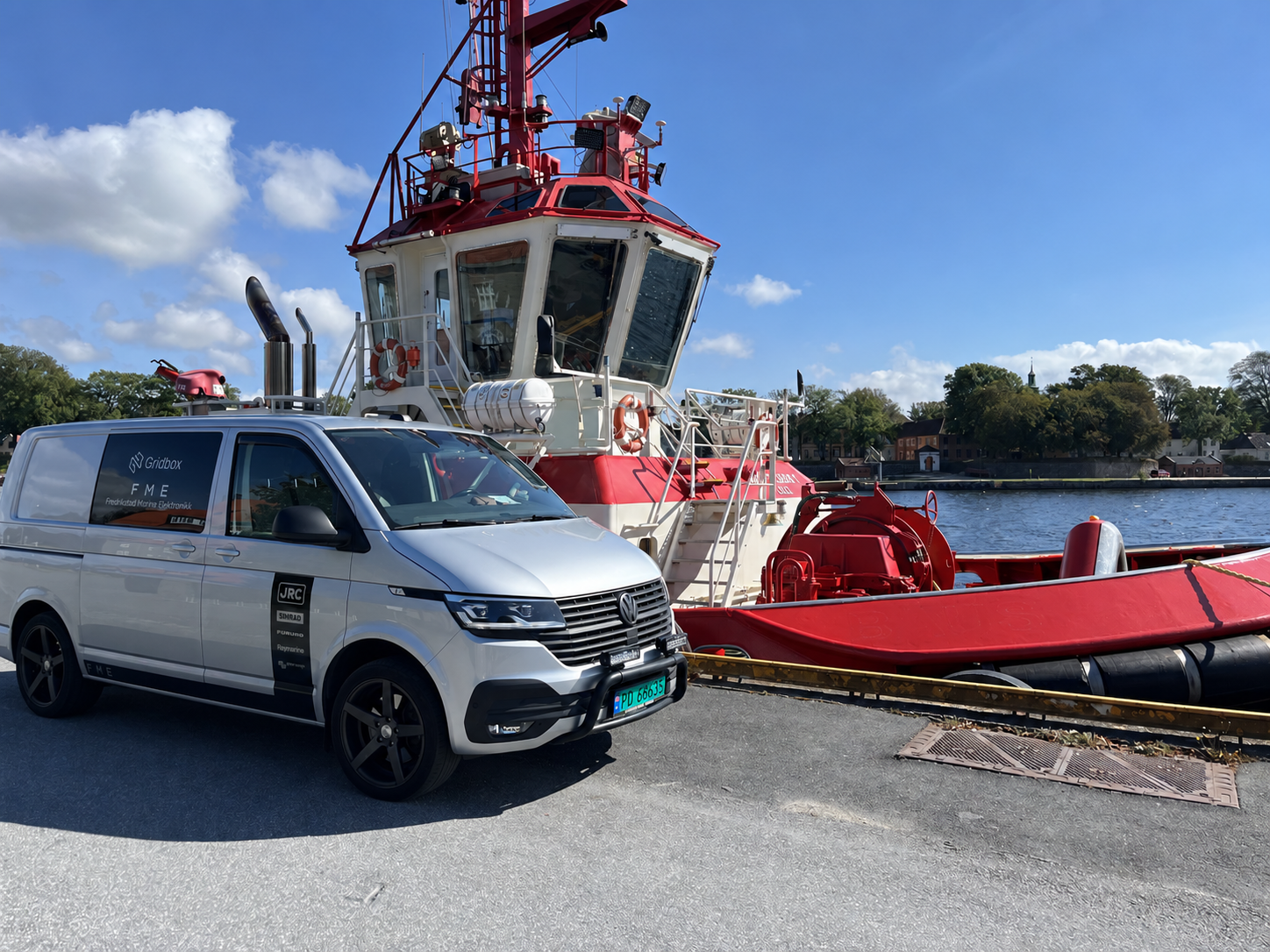 Fredrikstad marine elektronikk servicebil på fredrikstad brygge parkert ved siden av en rød og hvit taubåt som heter Baus