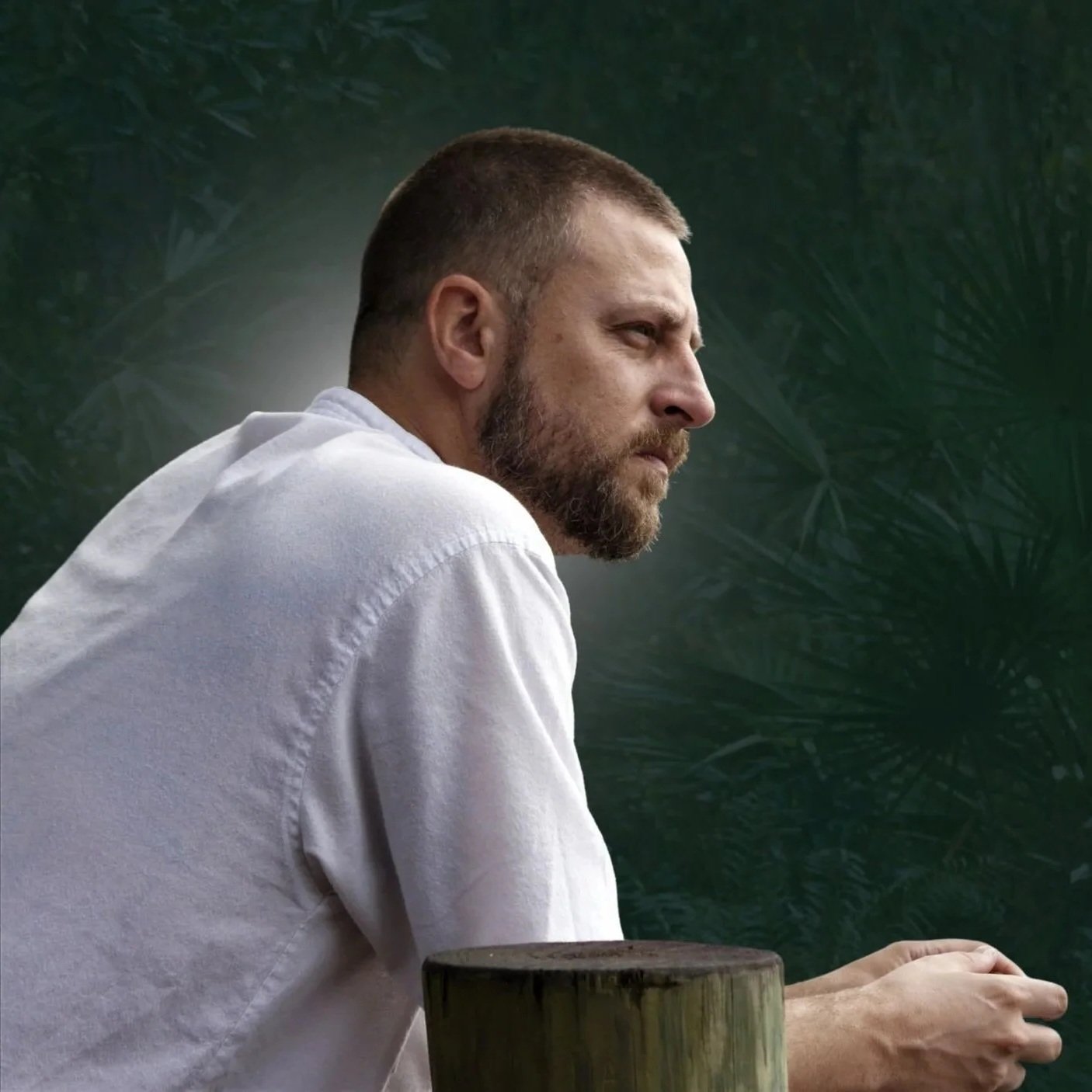 Andrew J. Assini spiritual guide in profile leaning against wooden post outdoors
