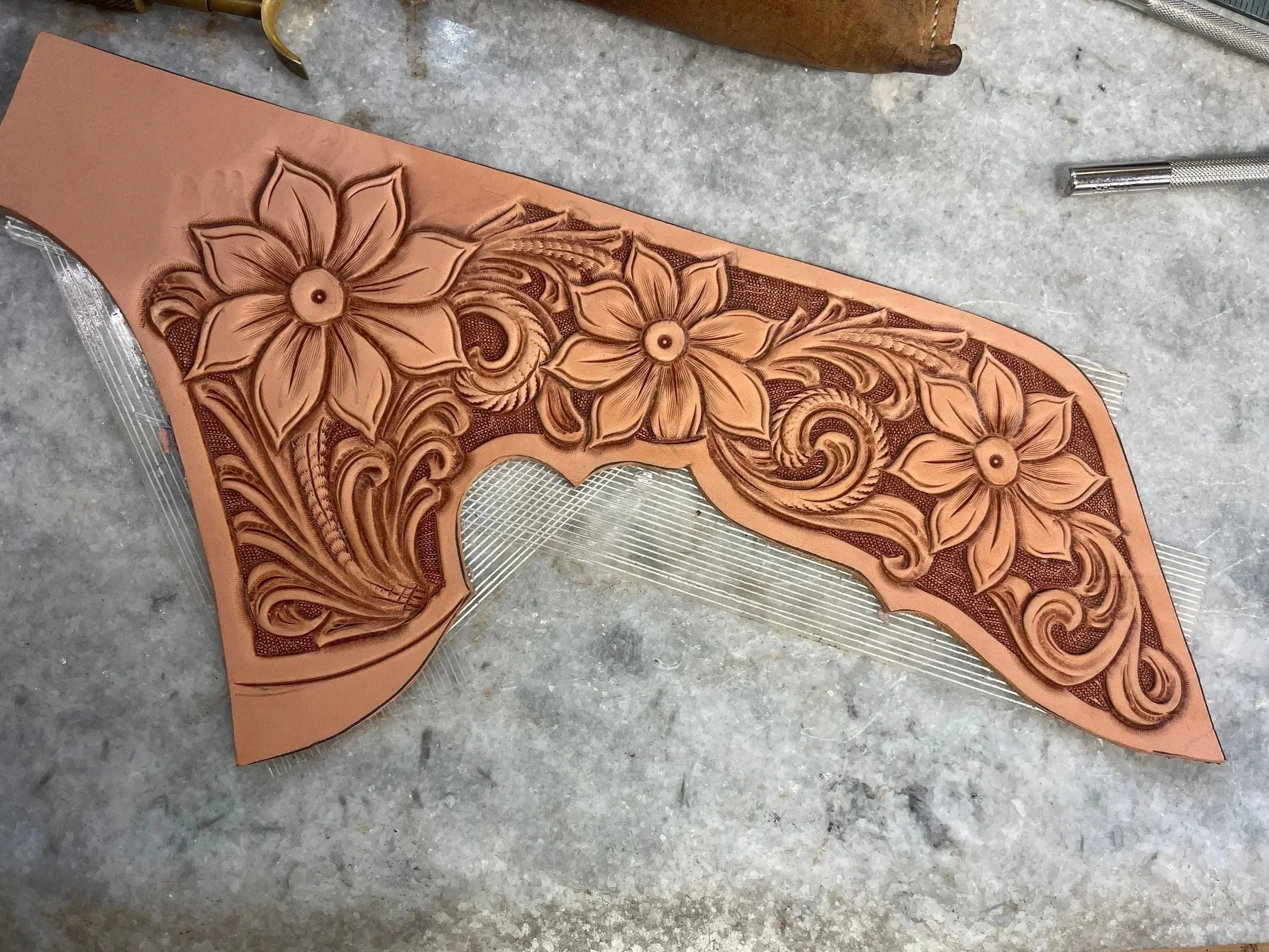 A leather stamping template with floral designs on a worktable with tools nearby.