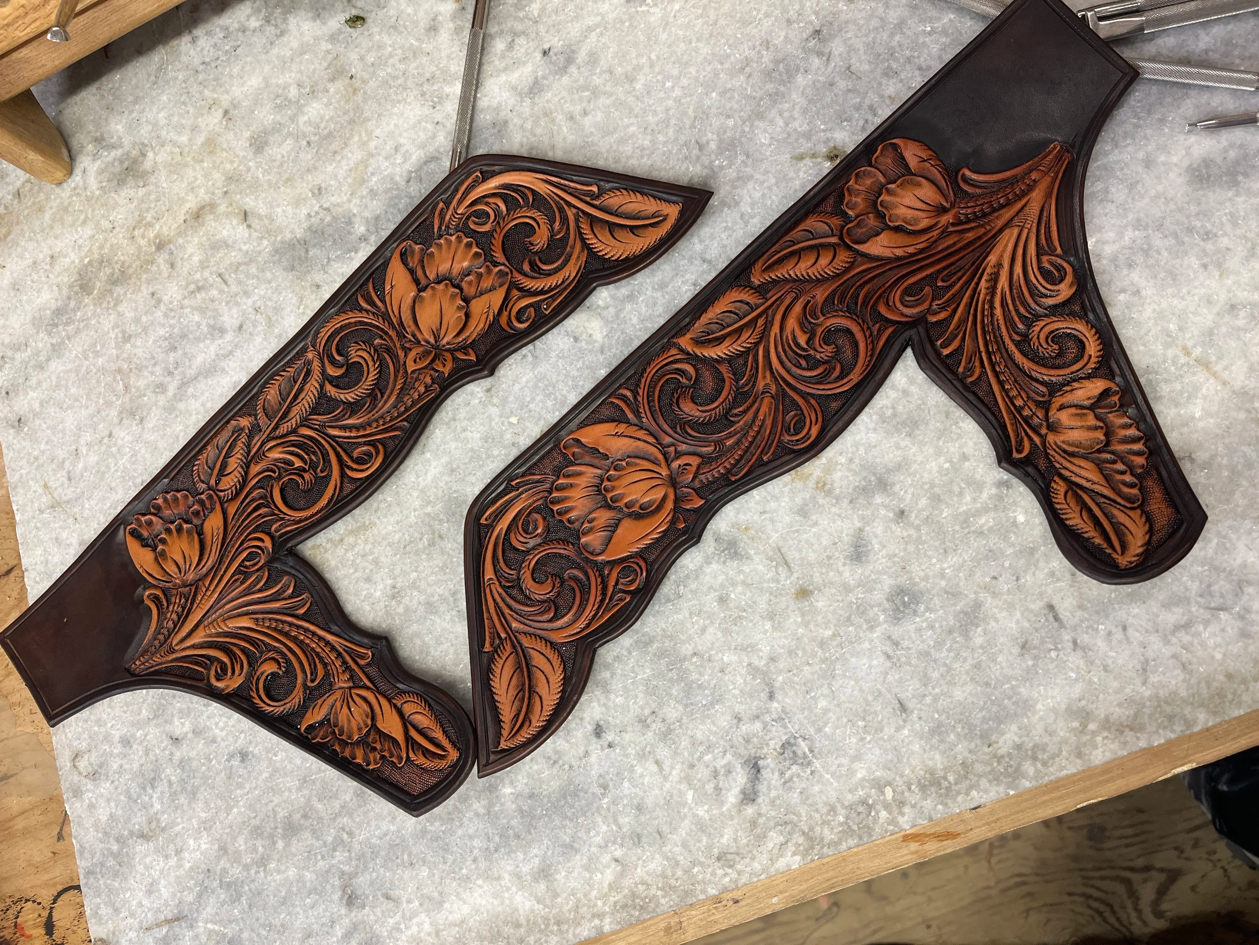 A wooden gun stock with intricate floral and leaf carvings, lying on a gray marble surface.