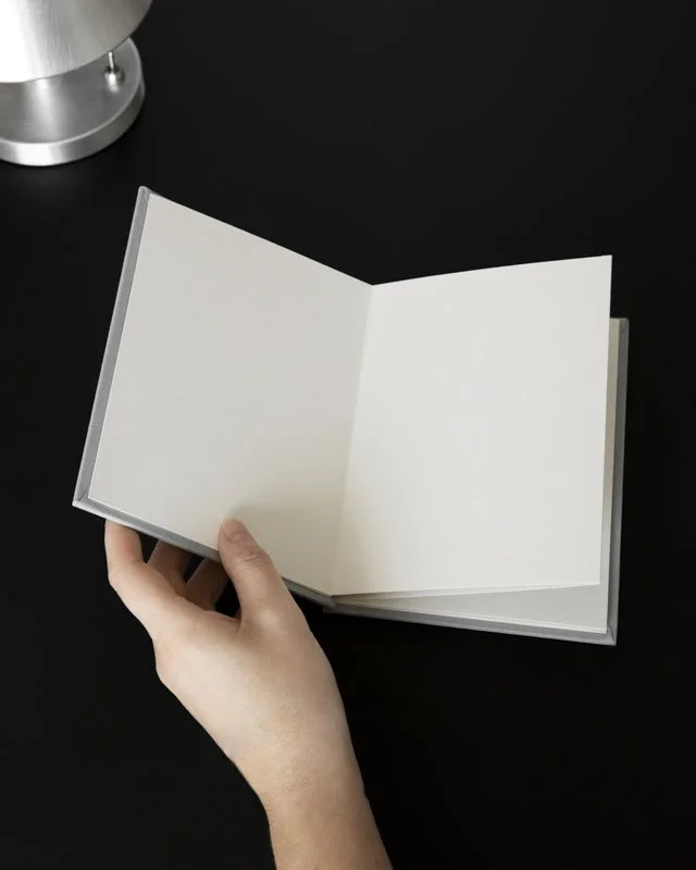A hand holding open a blank notebook against a black table.