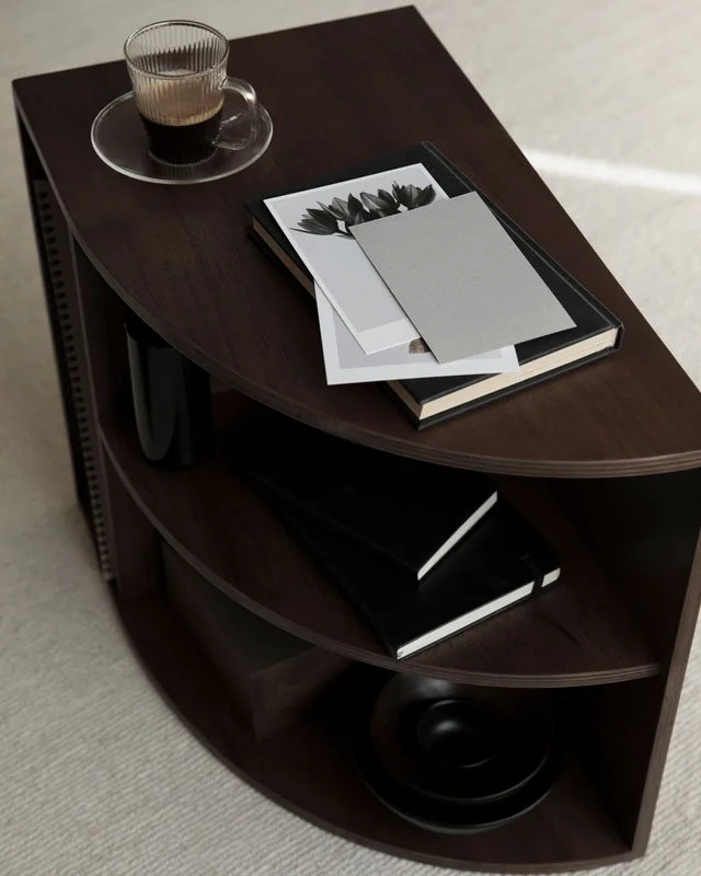 Dark wooden table with a glass of dark beverage on a saucer, and a stack of notebooks and papers on top.