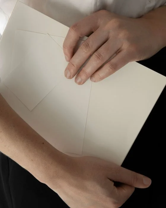 Person holding open blank white greeting card or poster board indoors.