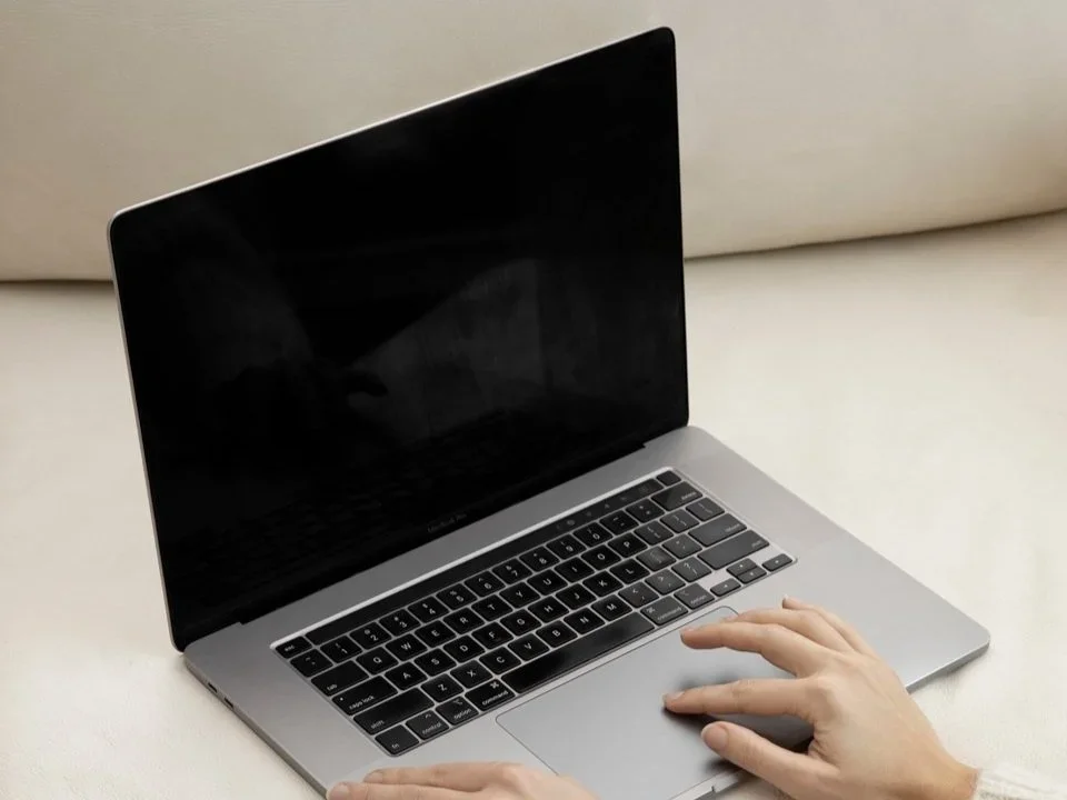 A person using a silver MacBook laptop on a white surface.