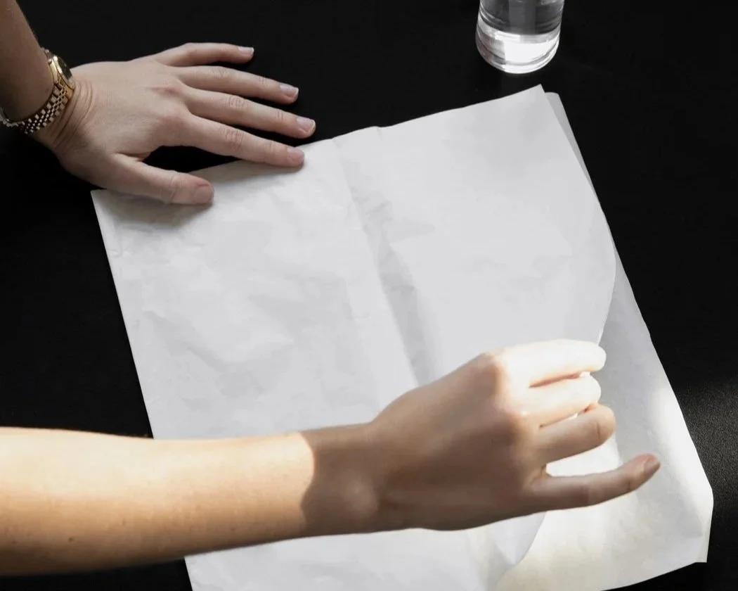Hands hold a crumpled piece of paper on a black background.