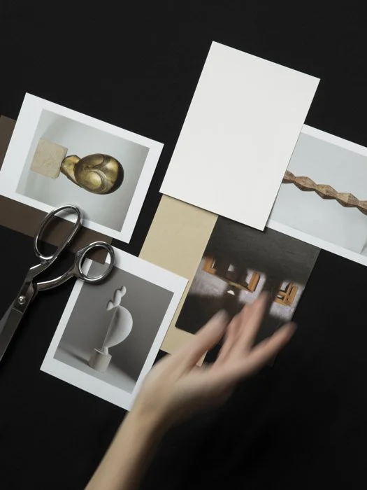 Overhead view of printed photographs and paper samples arranged on a dark surface, including abstract sculptural objects and interior details.