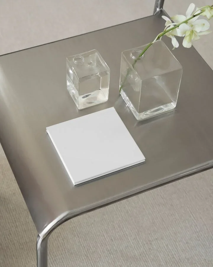 A stainless steel table with a vase with a white flower and paper.