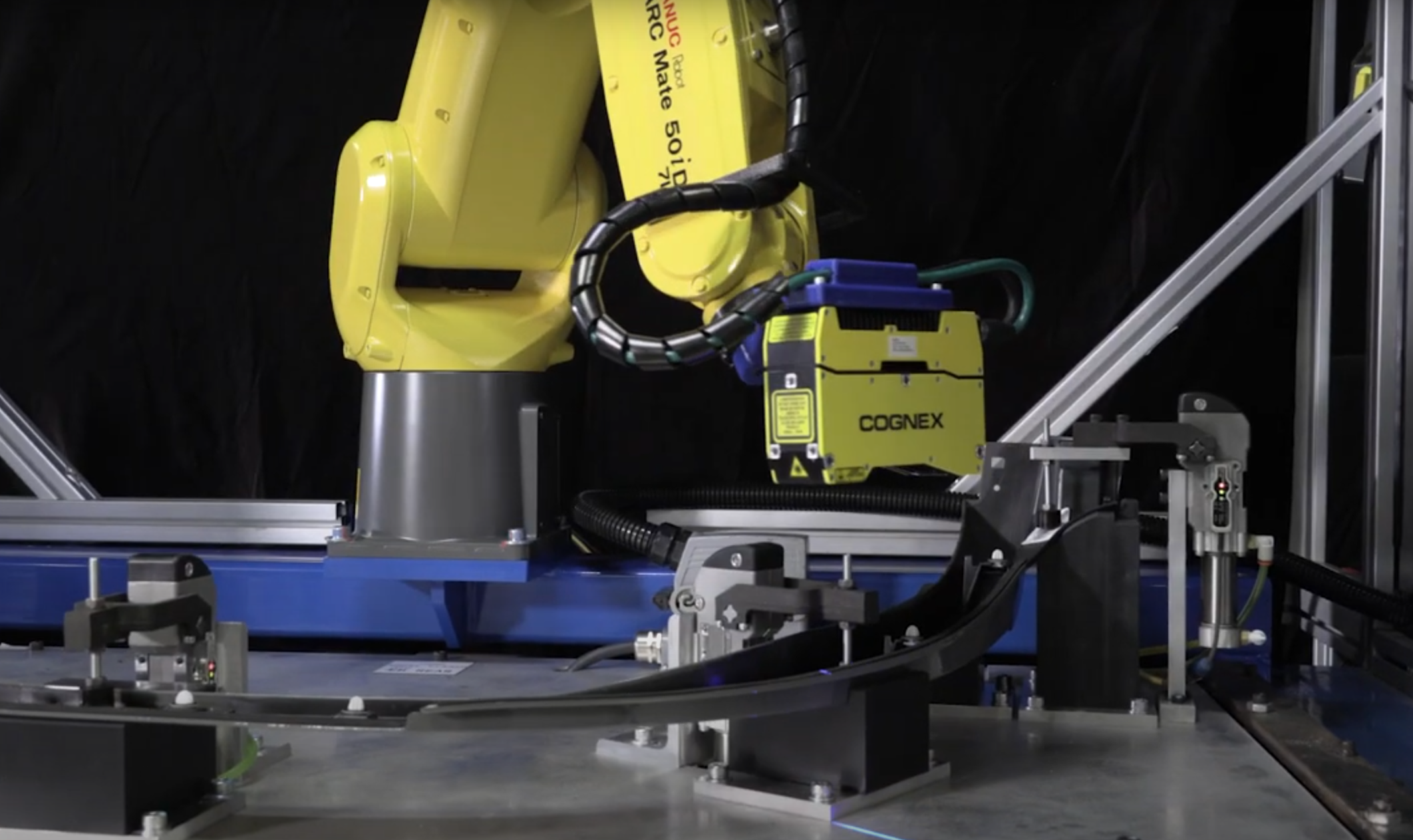 Industrial robotic arm labeled 'Fanuc ARC Mate 50iD' with a Cognex vision system, working on an automated assembly line with metal and plastic components.