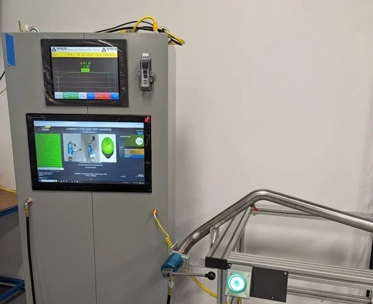 Industrial control panel with two screens displaying data and a metal frame beside it in a laboratory setting.