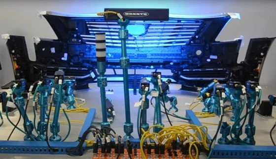 Automotive testing setup with instruments and cables in front of a car bumper.