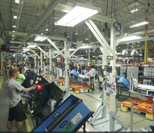 Employees working on vehicle assembly lines in a large, well-lit factory.
