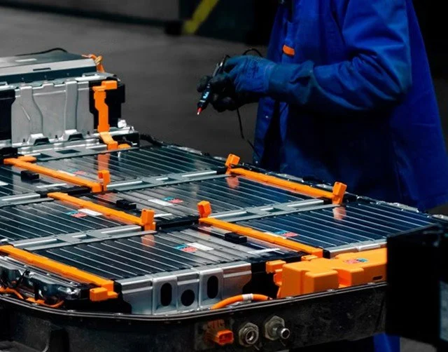 Technician in blue uniform working on a large battery pack with orange and gray components in a technical setting.