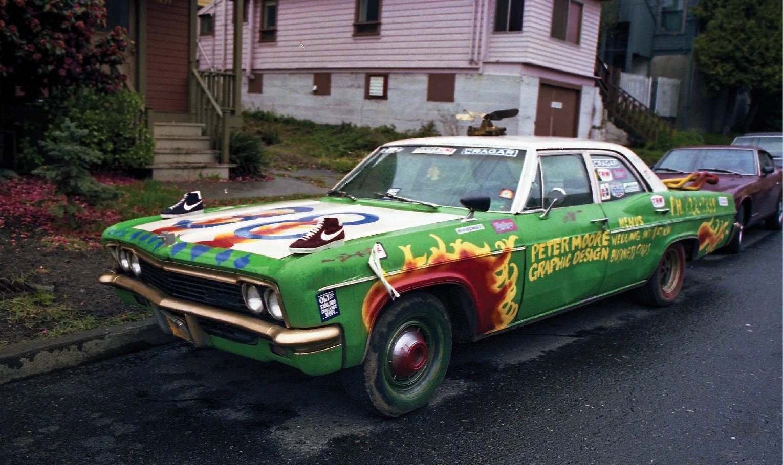 A green and white car with flames painted on it, Nike shoes mounted to the hood, and the words "Peter Moore Graphic Design"