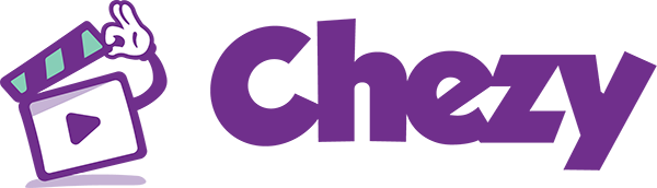 A man wearing safety glasses, a yellow helmet with the Habitat for Humanity logo, and a T-shirt with a Habitat for Humanity logo, is hammering a nail into a wooden structure outdoors on a sunny day.