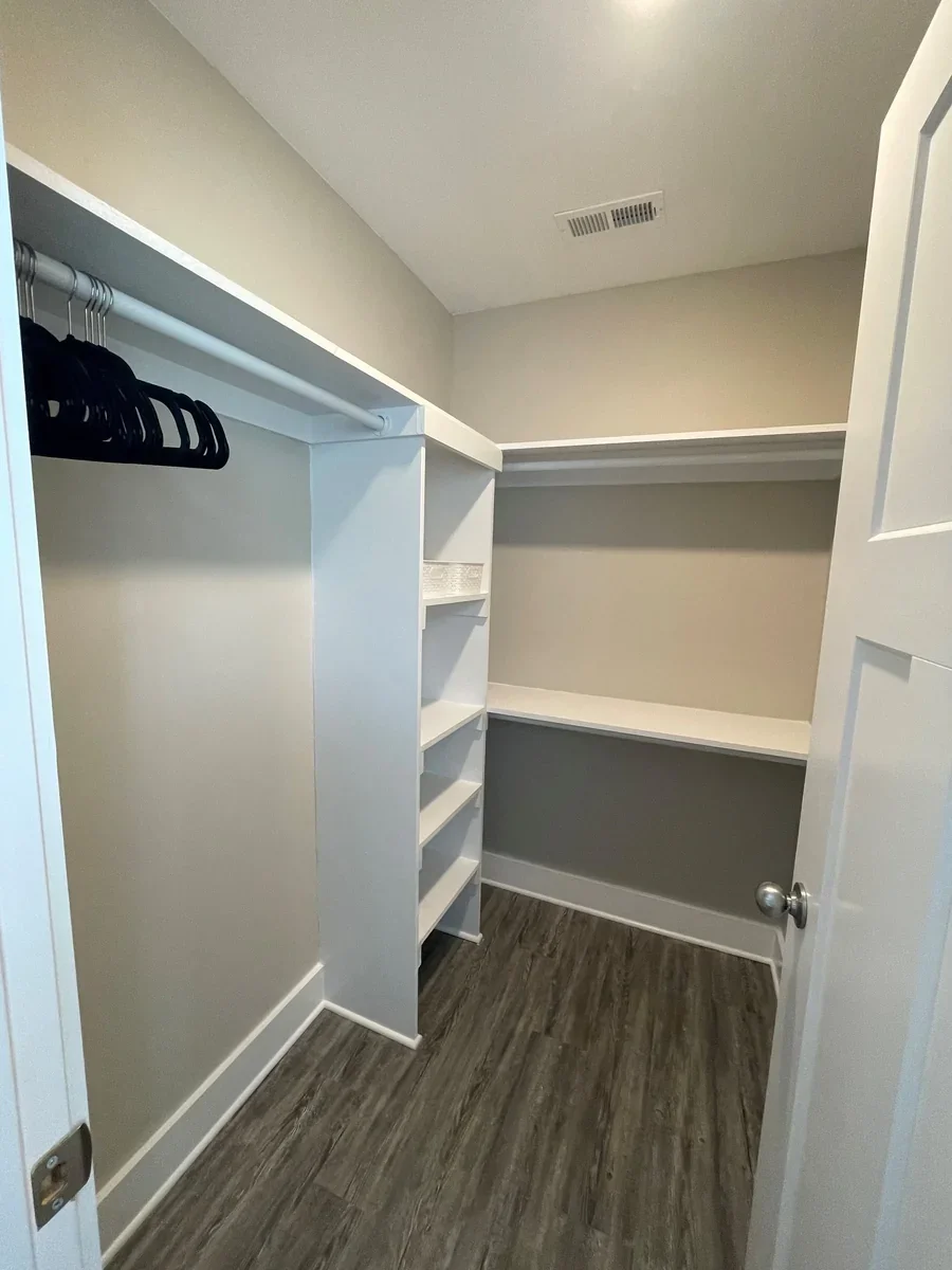 Empty walk-in closet with white shelving, black hangers, and laminate wood flooring.
