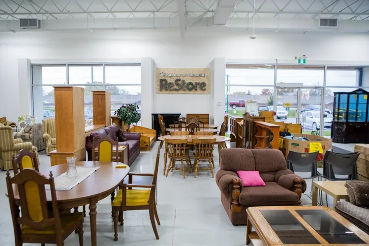 Interior of a furniture store with various chairs, sofas, and tables, and a sign that reads 'Habitat for Humanity ReStore' on the wall.