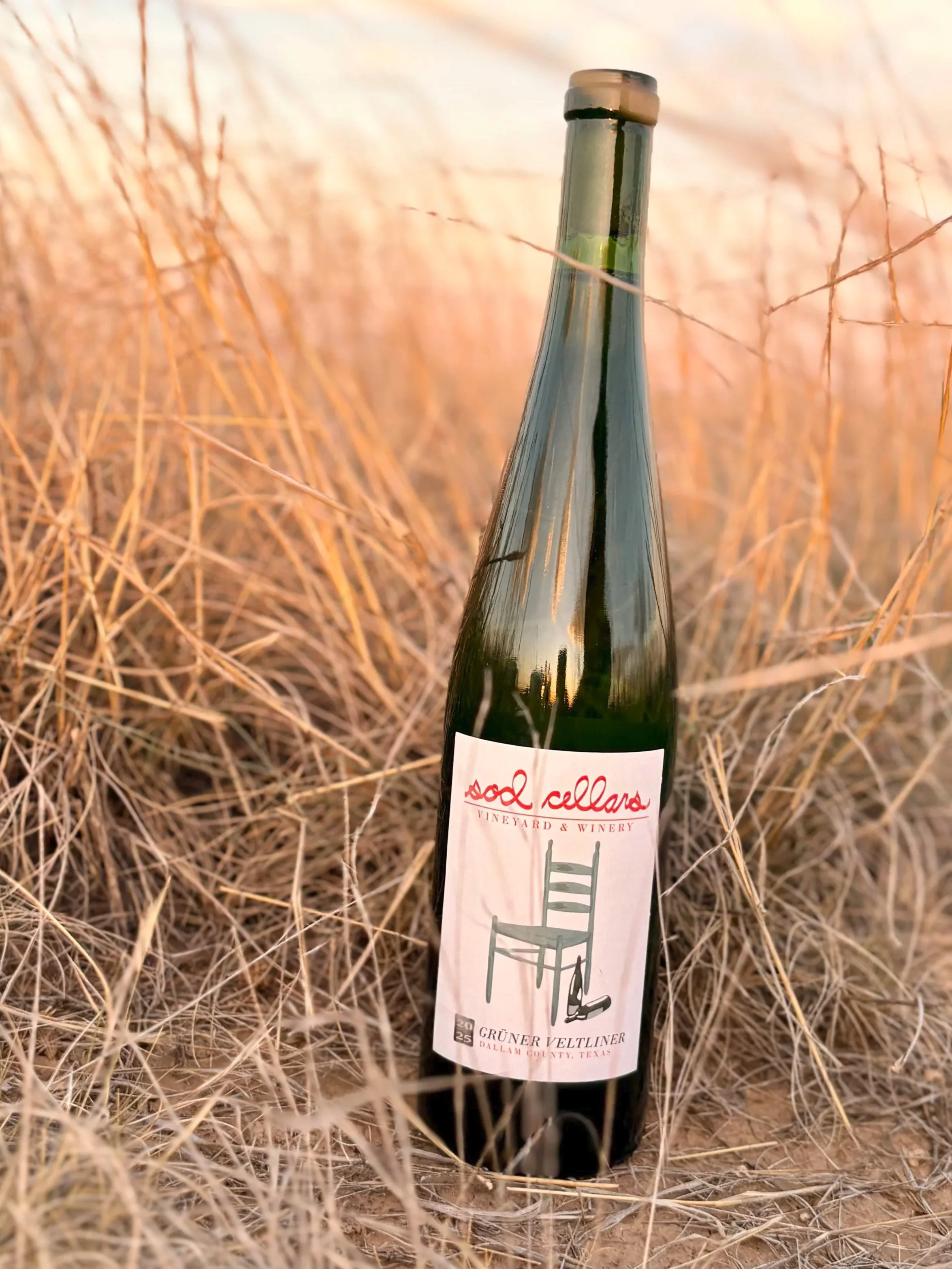A bottle of Sod Cellars Gruner Veltliner placed among dry grass.