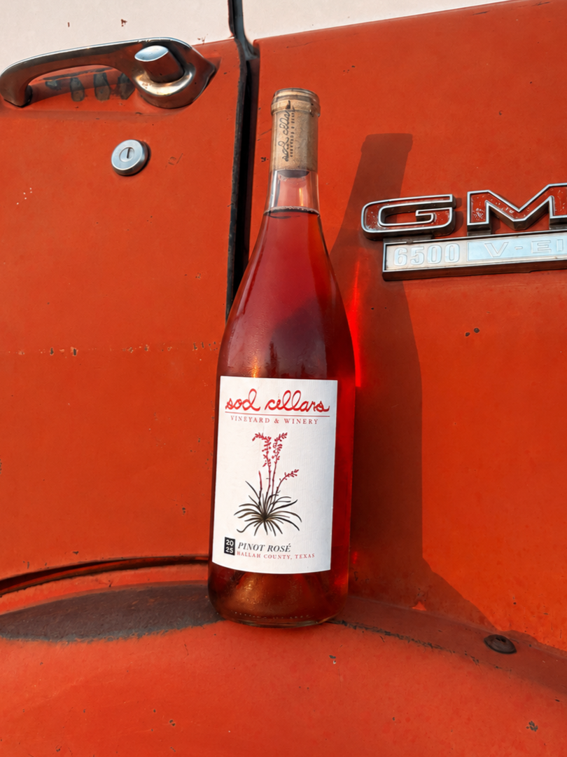 A bottle of Sod Cellars Pinot Rosé wine resting against the side of a GMC vehicle.
