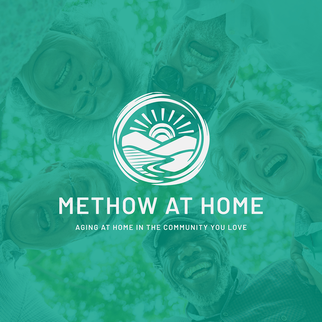A group of elderly people looking down at the camera and smiling, with a logo of a sunset over mountains and water in the center, and the text "Method at Home, Aging at Home in the Community You Love" below.