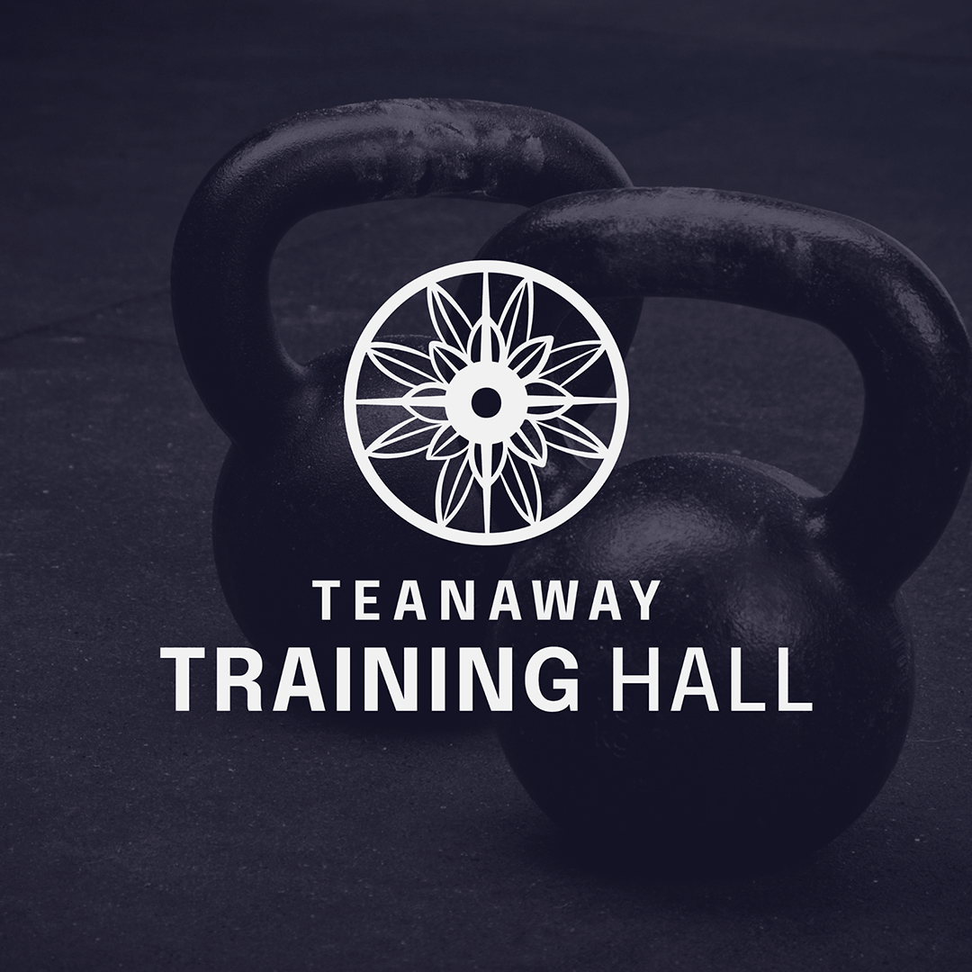 Black kettlebells on a dark gym floor with white logo and text for Tattooaway Training Hall.