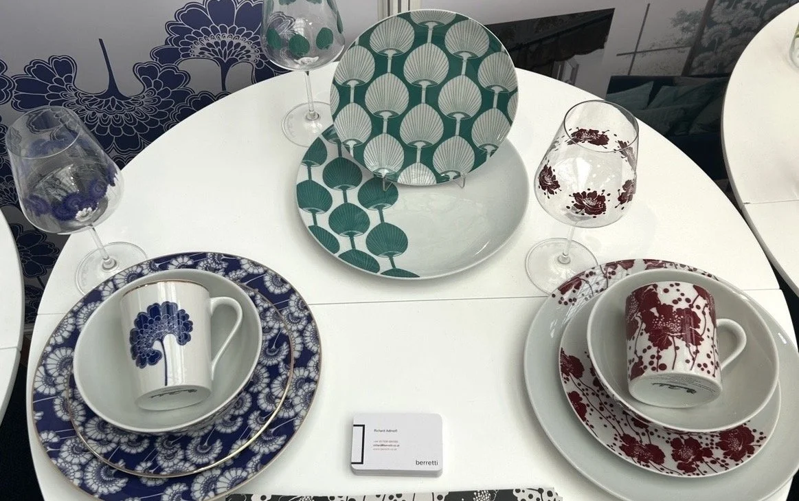 A round white table set with dinnerware and glassware. Two tea cups and matching saucers with blue and red floral patterns are placed on the table.