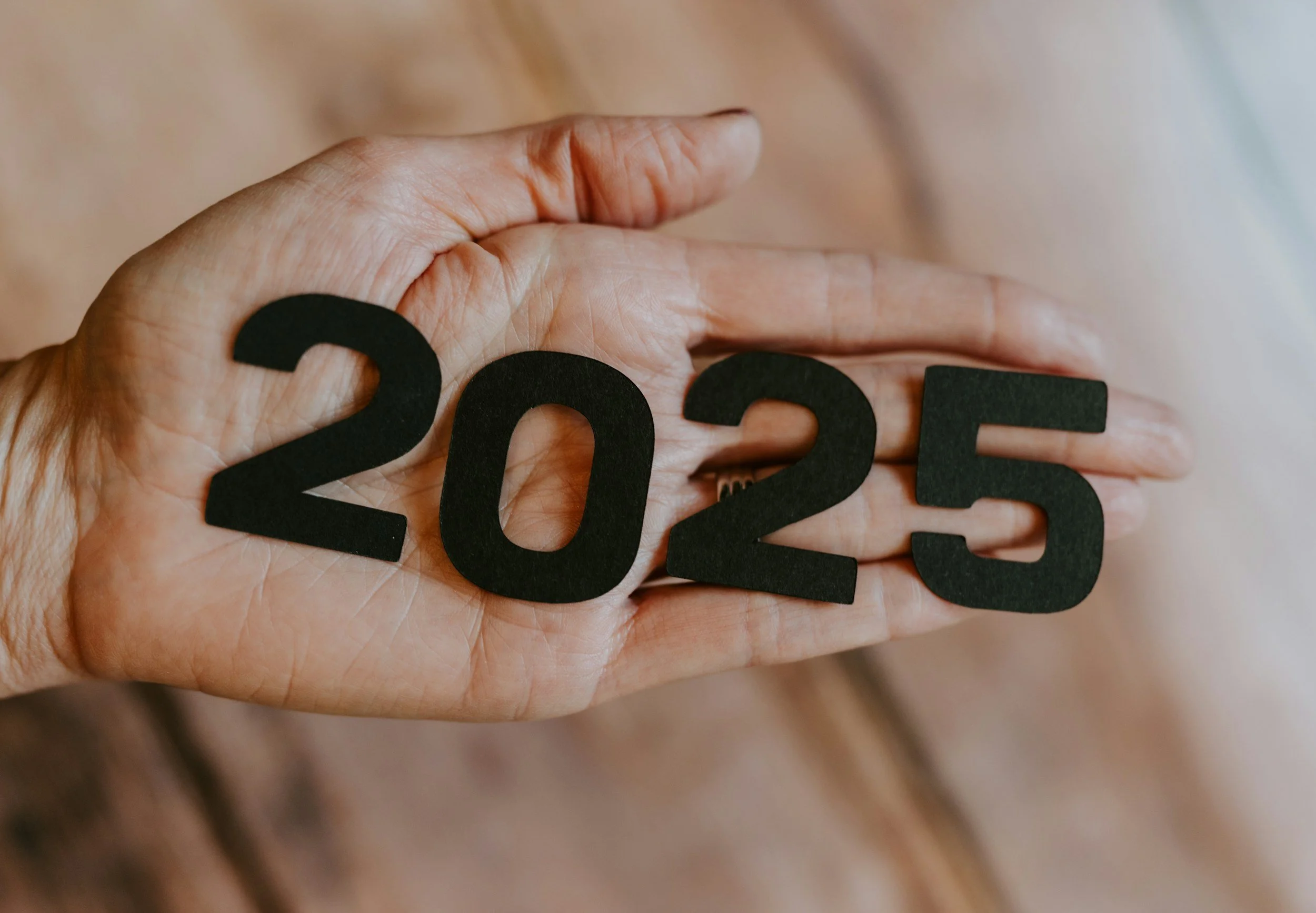 A hand holding '2025', symbolizing new year goals and growth for TheraSistersSTL's reflection guide.