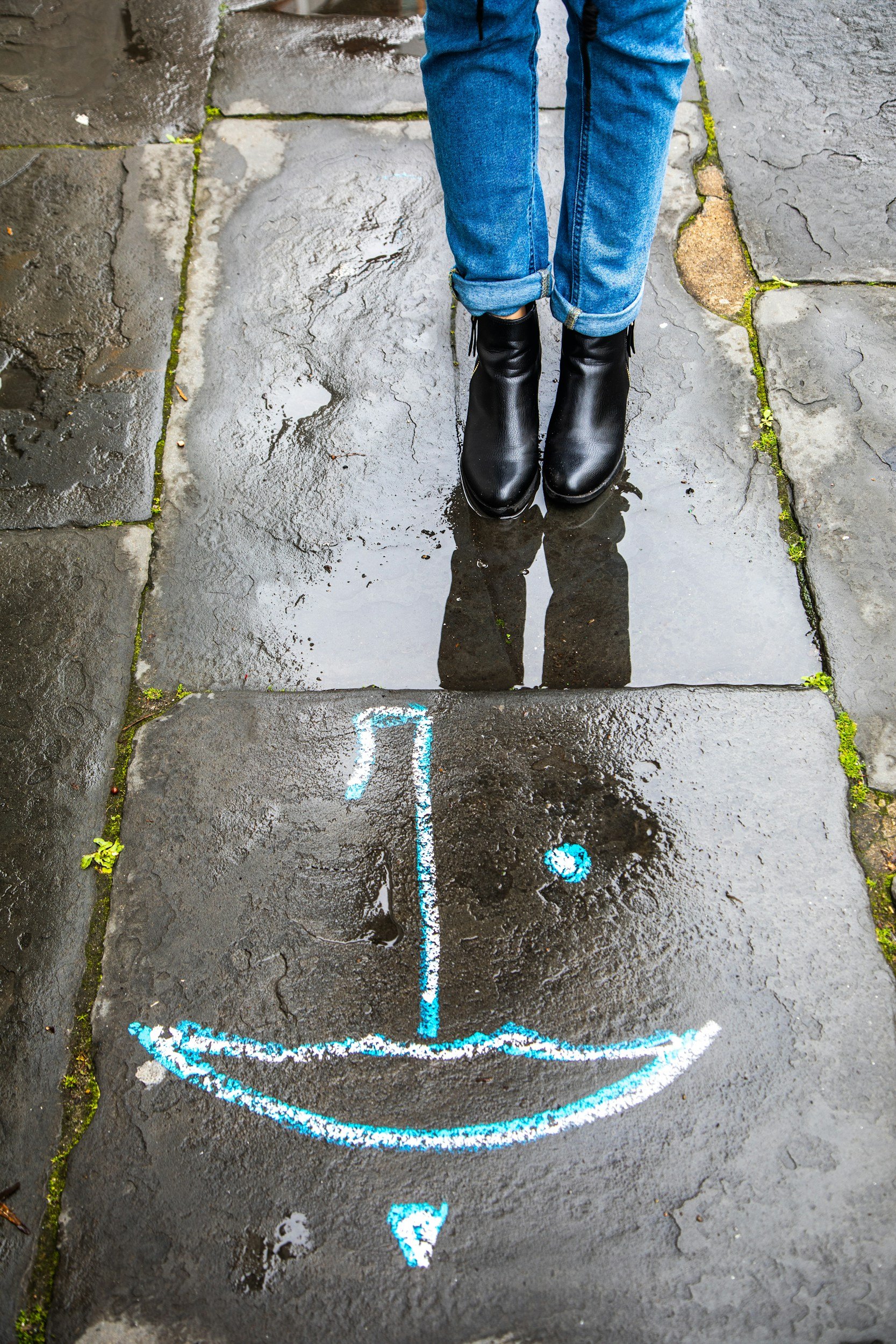 Embracing life's messiness: A person stands over a puddle's chalk art, finding self-support in unexpected moments.