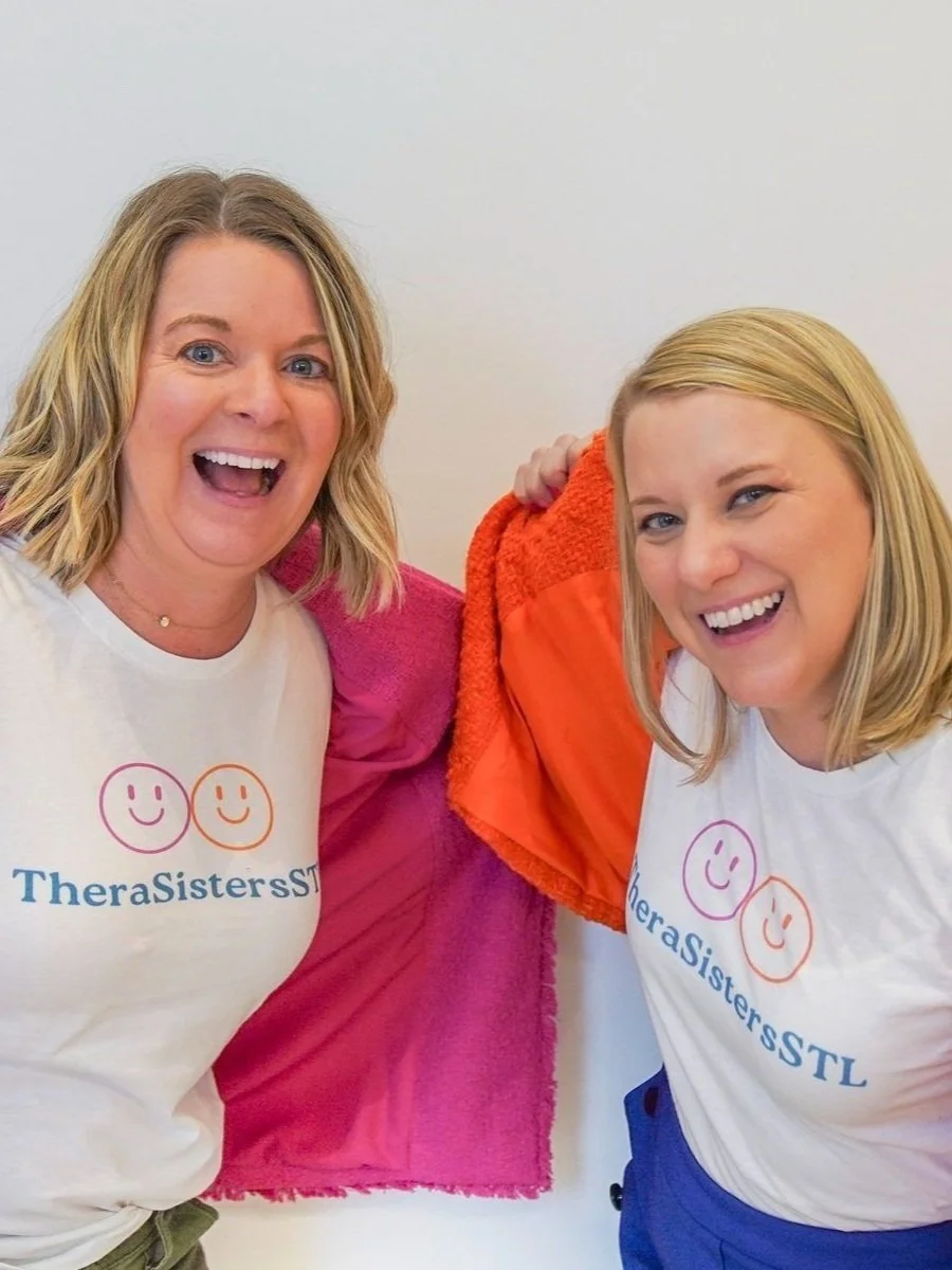 Amy and Katheryn, the founders of TheraSistersSTL, smiling brightly in their branded t-shirts, representing their mission to bring joy and support to therapists and healers.