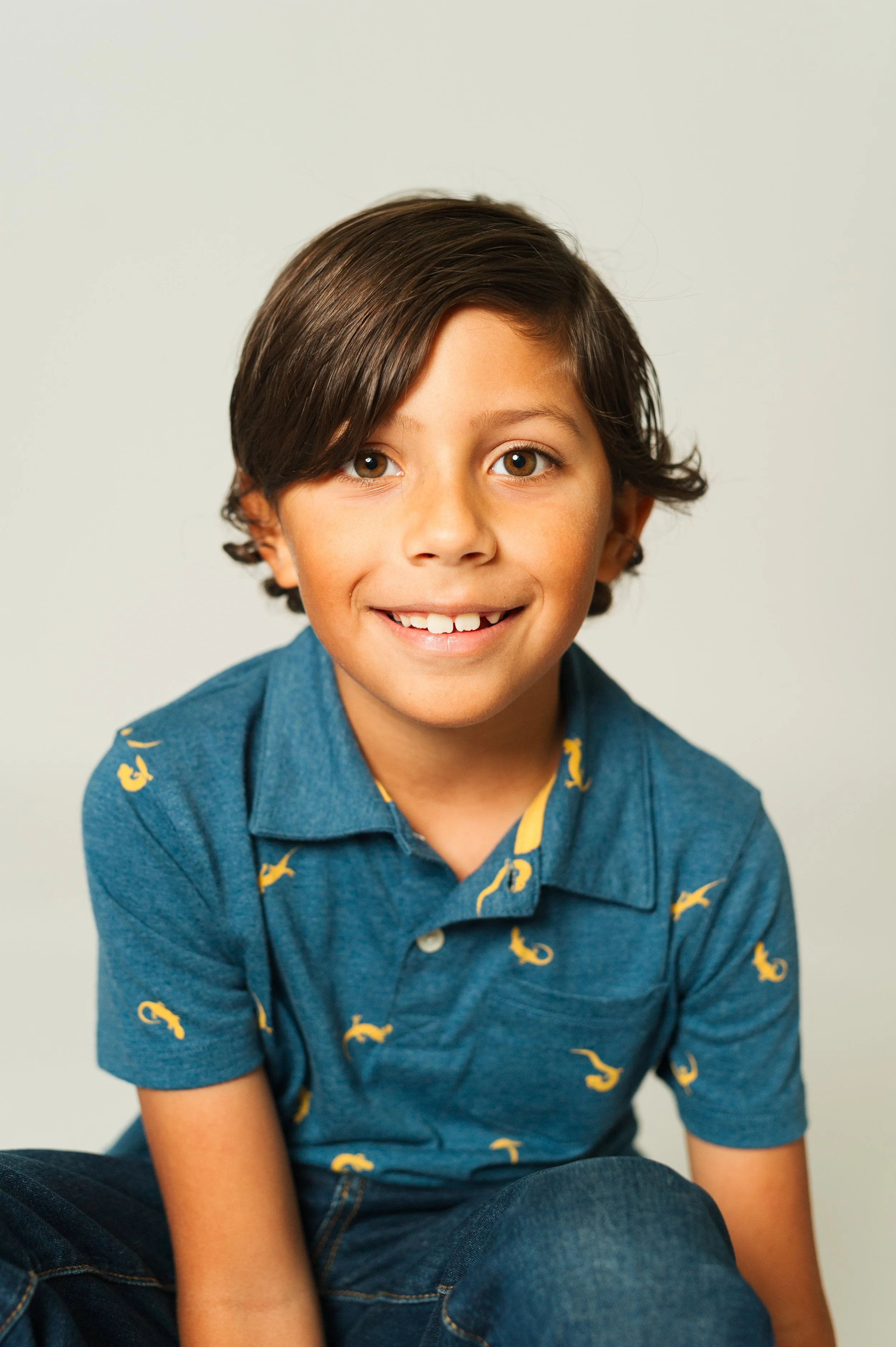 Smiling child wearing a blue shirt with yellow seahorse patterns.