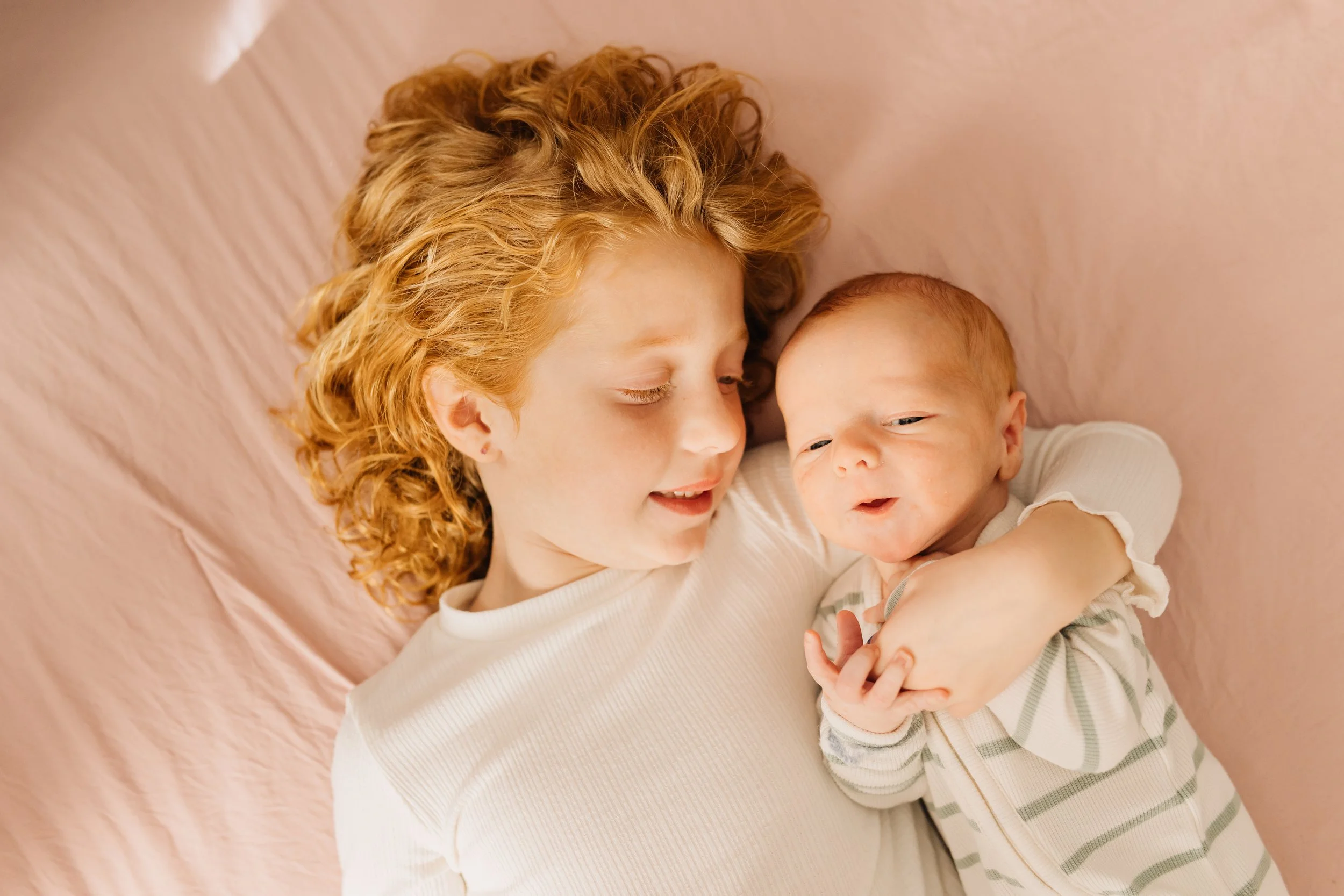 big sister and newborn snuggling newborn in home lifestyle session OKC
