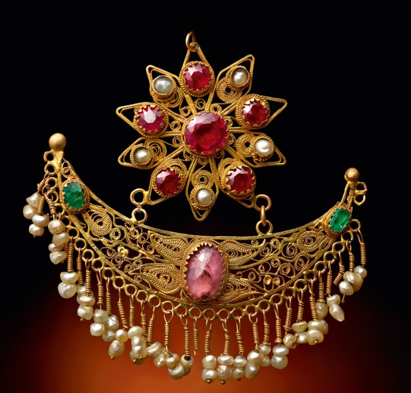 Gold jewelry set with red and white gemstones, featuring a brooch with a red central stone, a crescent-shaped necklace with pink and green stones, and pearl accents.