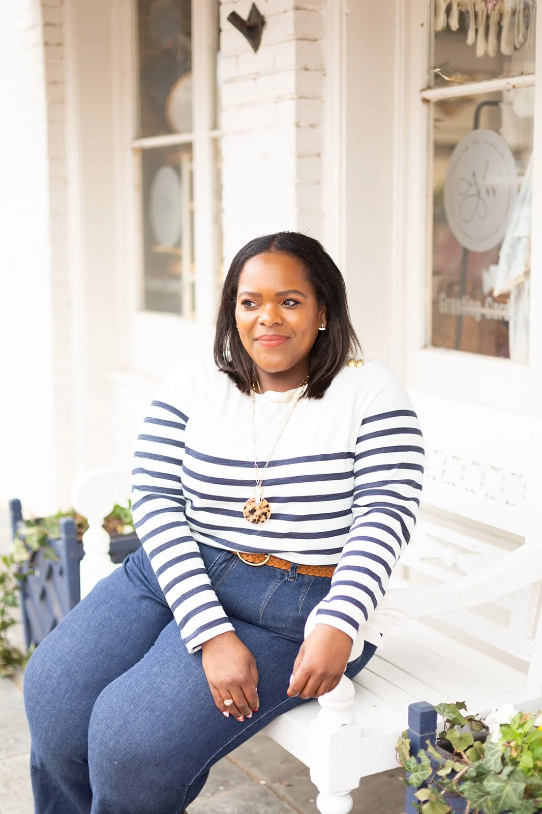 Person sitting on a white bench wearing a striped sweater and jeans, outdoors.