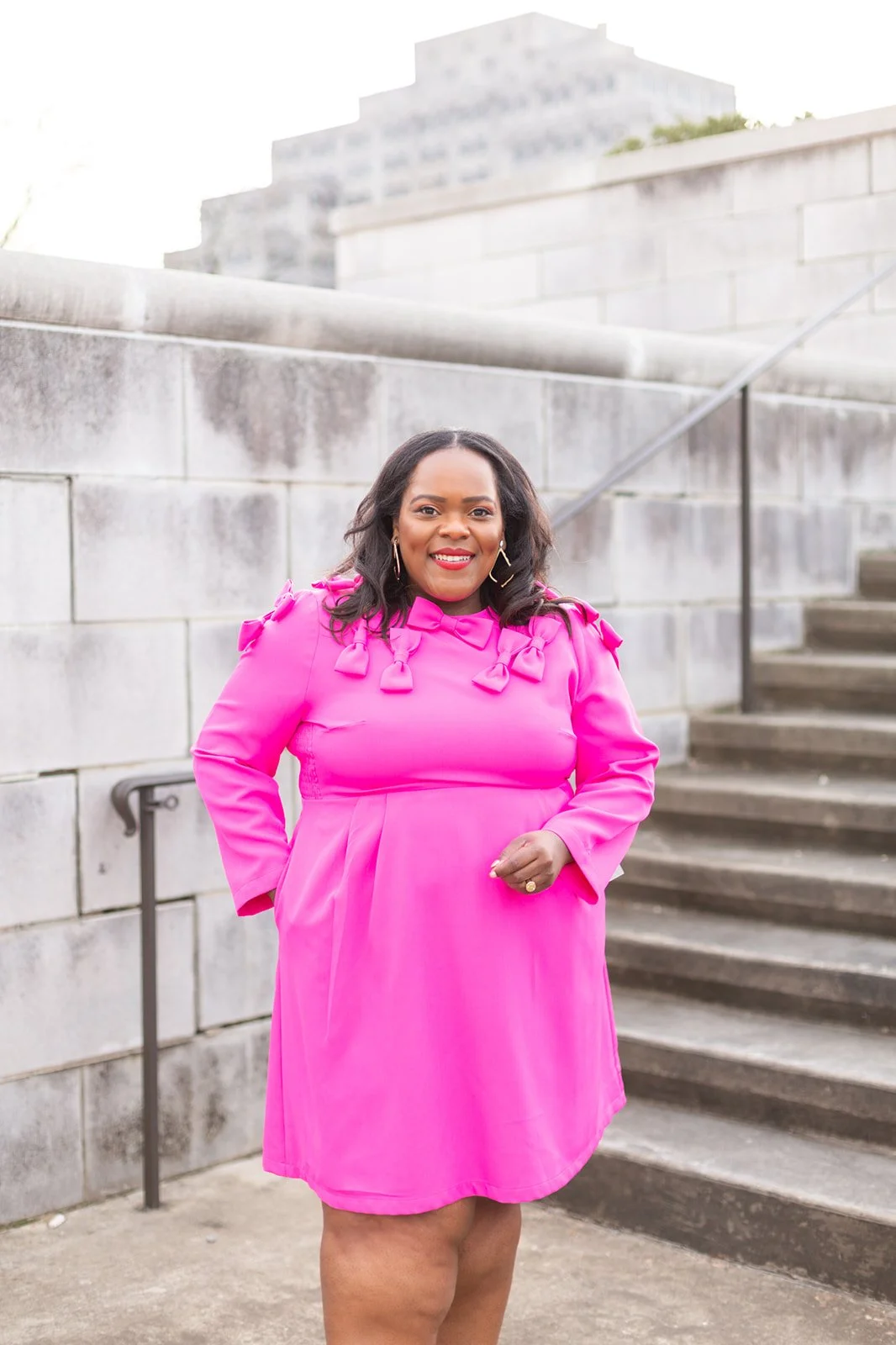 A person in a bright pink dress standing near stone stairs outdoors.