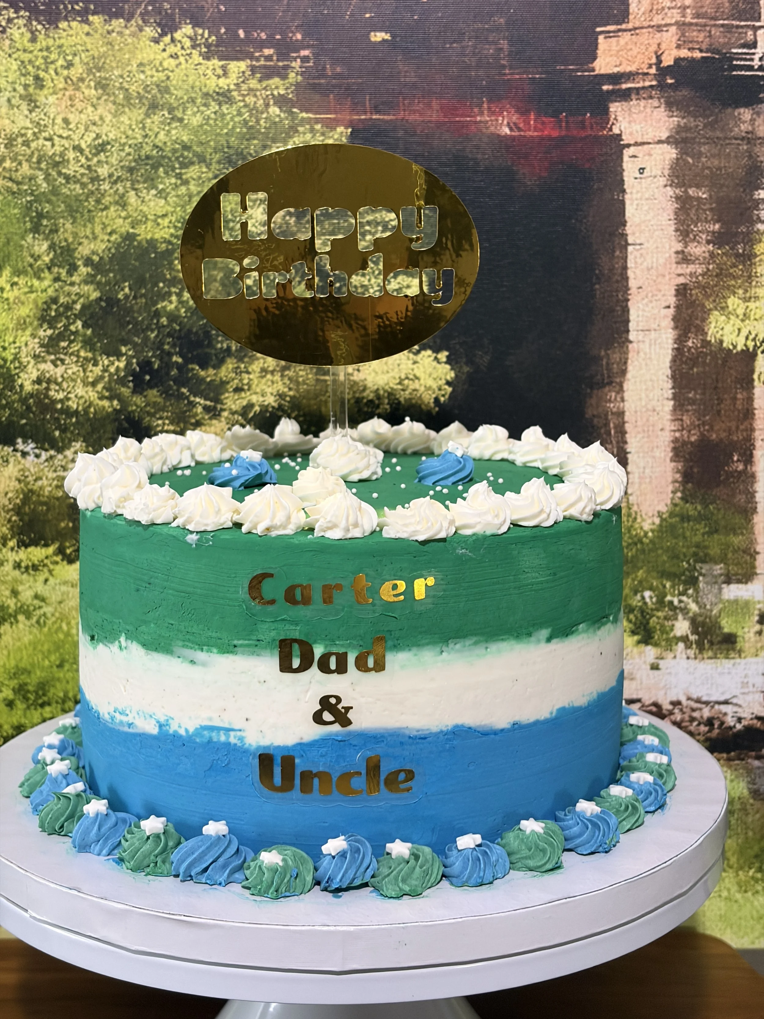 Blue, white and green ombre buttercream icing, on a cake that reads 'Happy Birthday' Carter, Dad & Uncle.