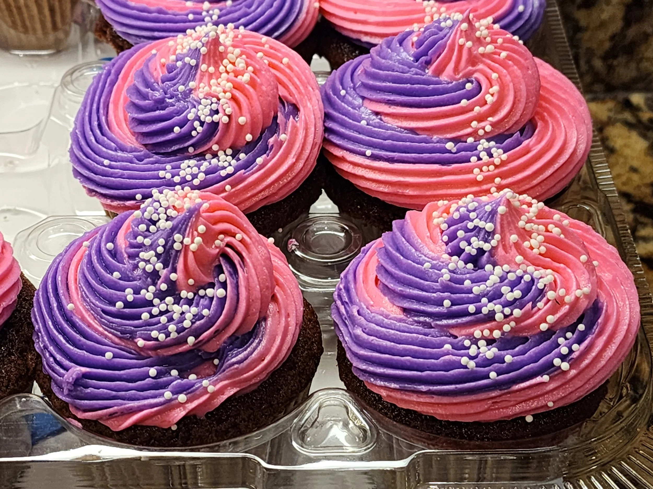 Chocolate cupcakes with pink and purple swirled frosting, topped with white pearl sprinkles