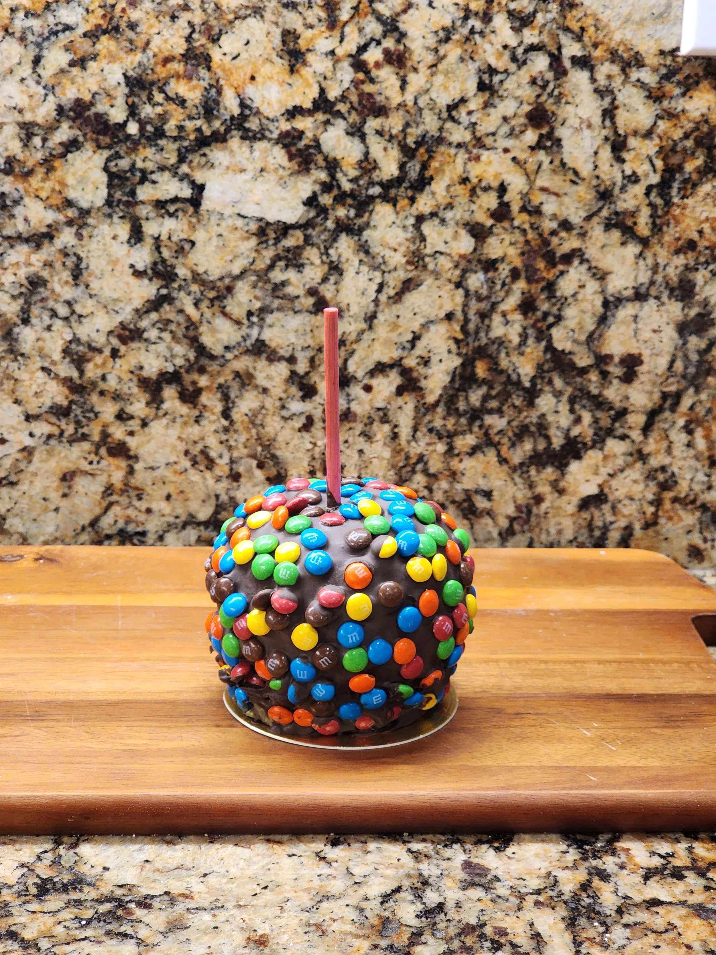 A caramel apple covered in colorful candy pieces resembling M&Ms.