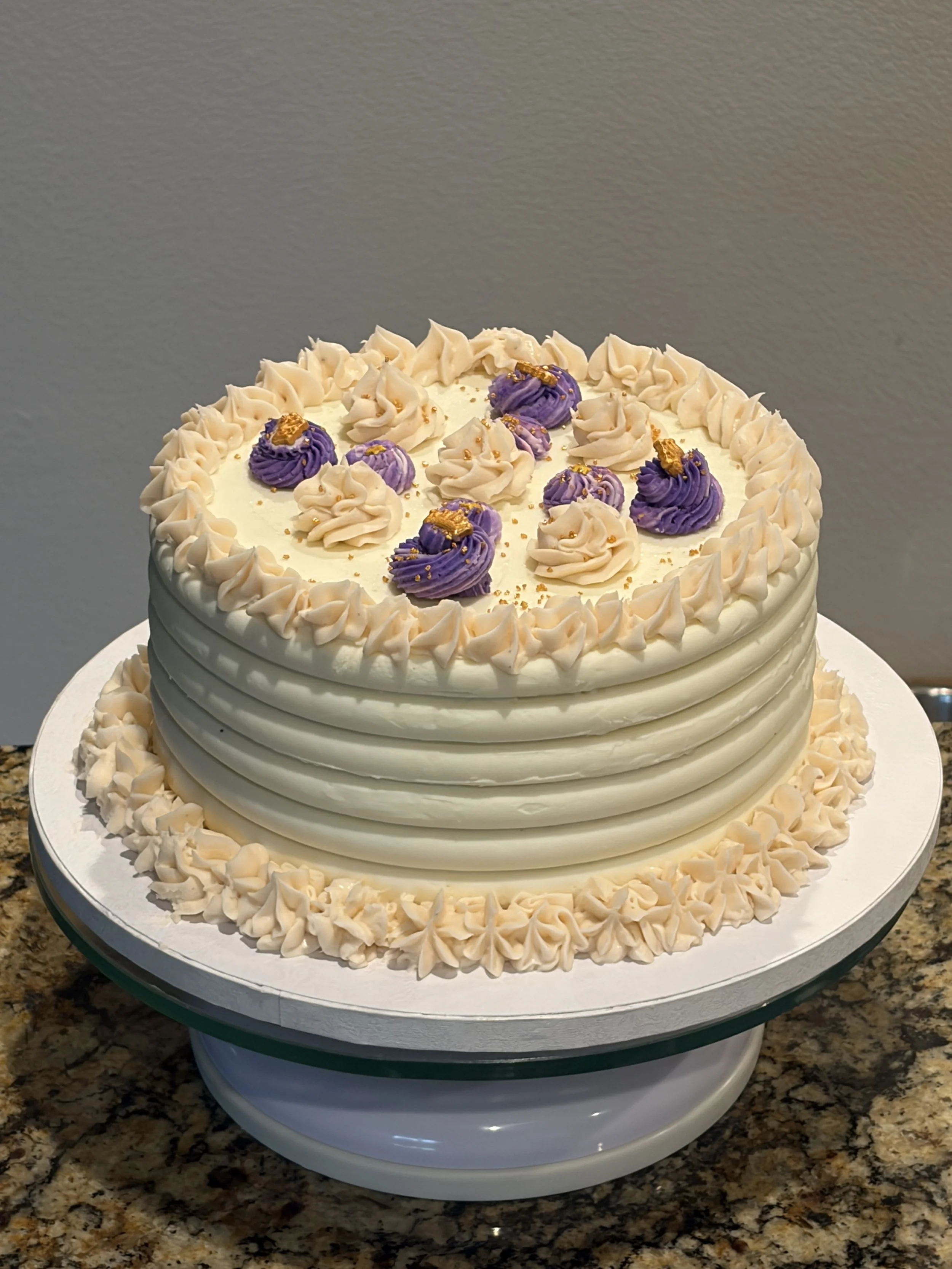 9-inch cake coated in crumb topping with purple sugar flower accents, on a cake stand