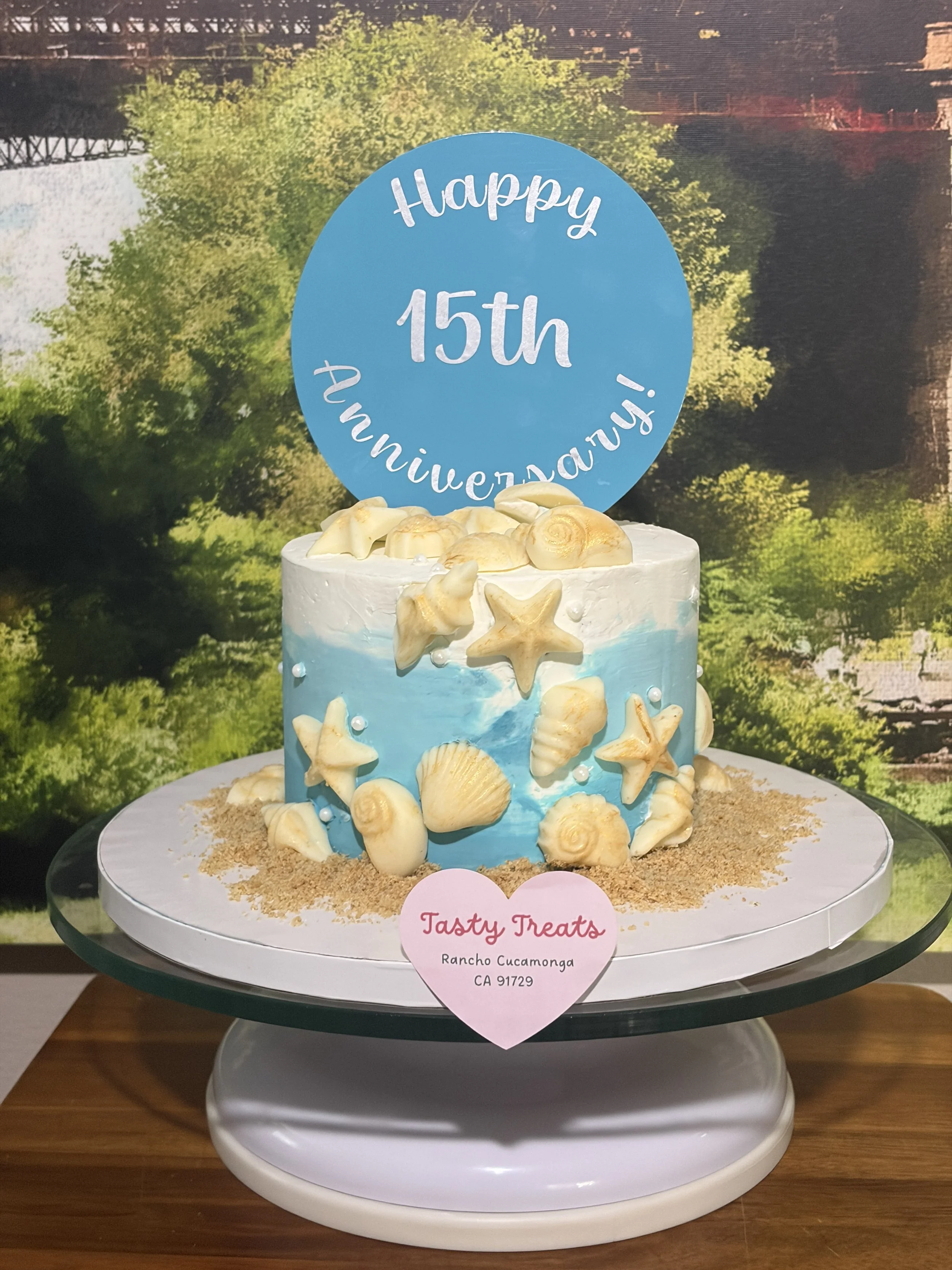 Teal and white 6-inch cake with a "Happy 15th" topper, displayed on a cake stand with cookies