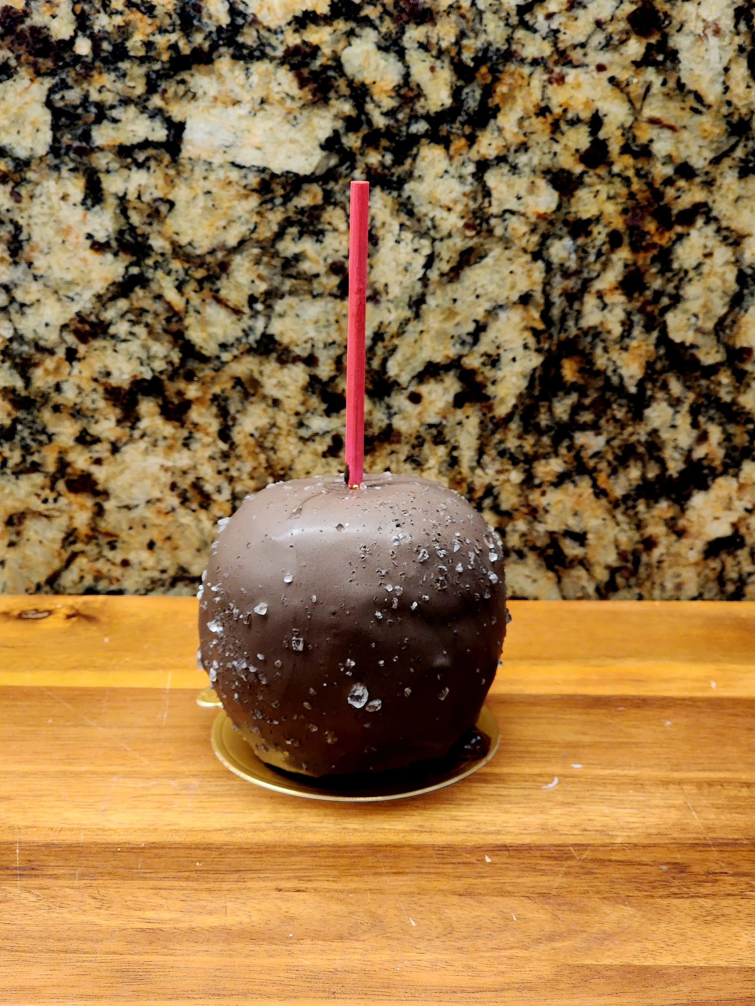 A caramel apple dipped in dark chocolate with a speckled drizzle.