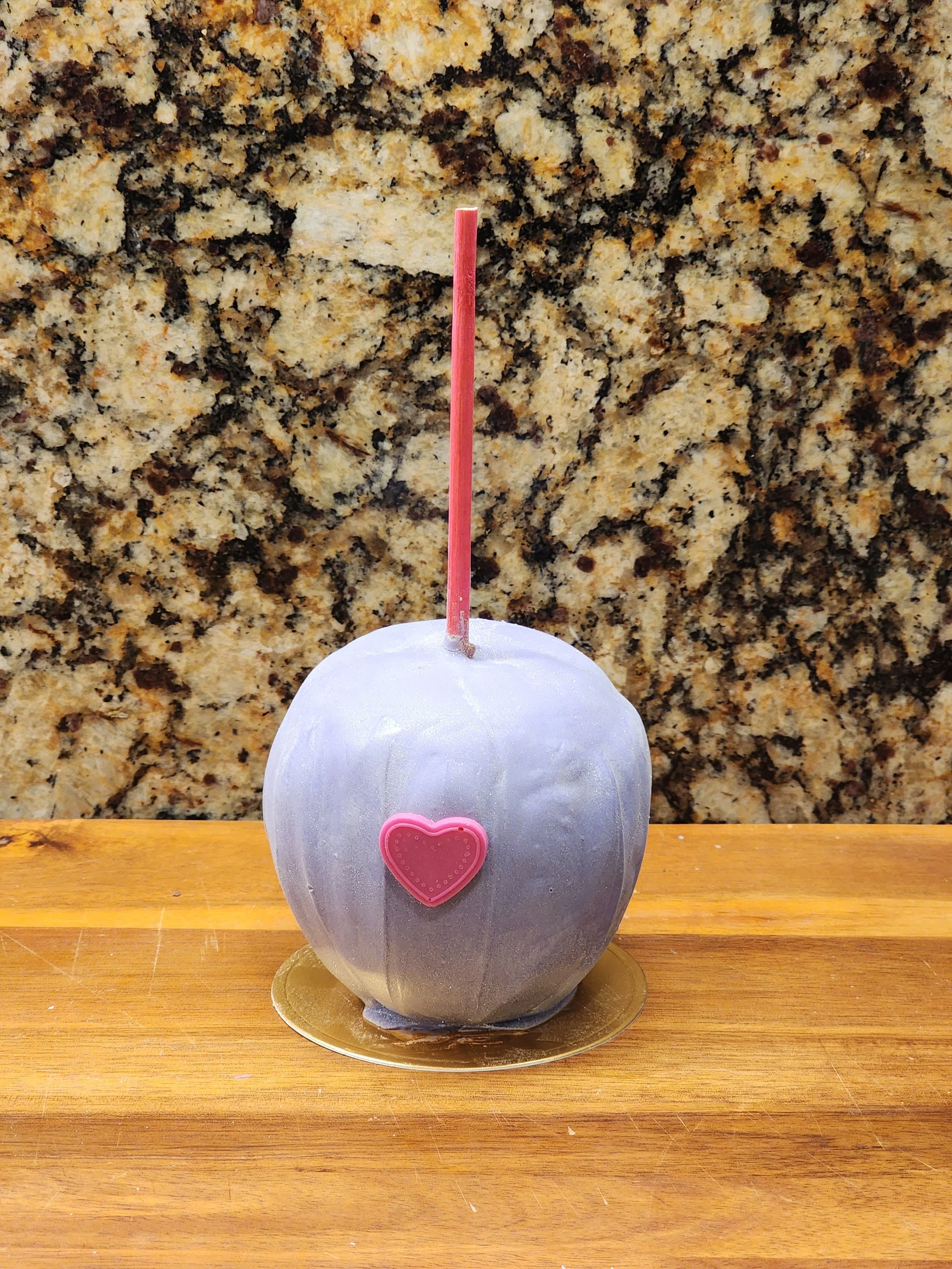 A caramel apple covered in light blue sanding sugar with a pink heart candy.
