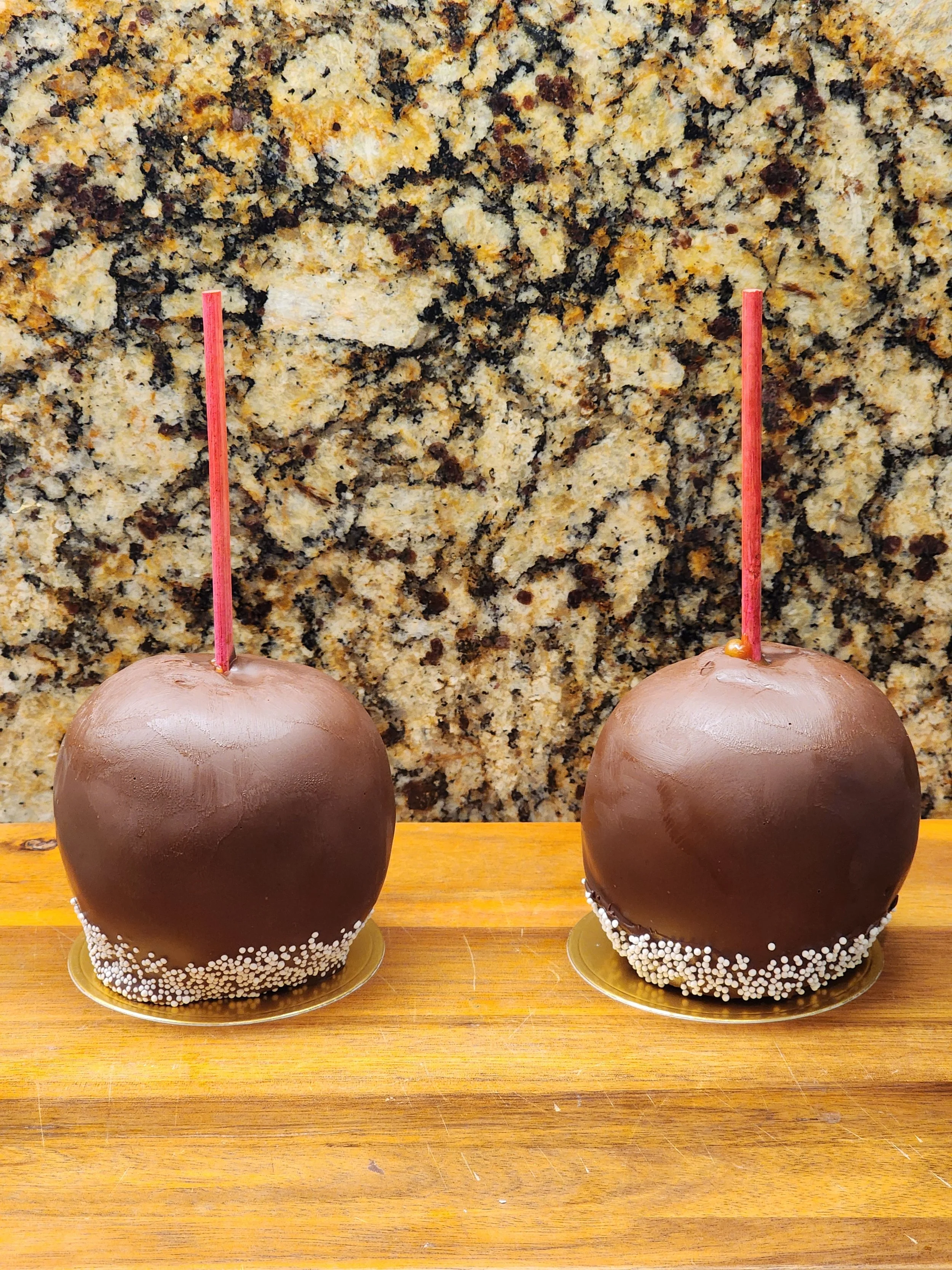 Two caramel apples dipped in dark chocolate with a sprinkle-coated rim.