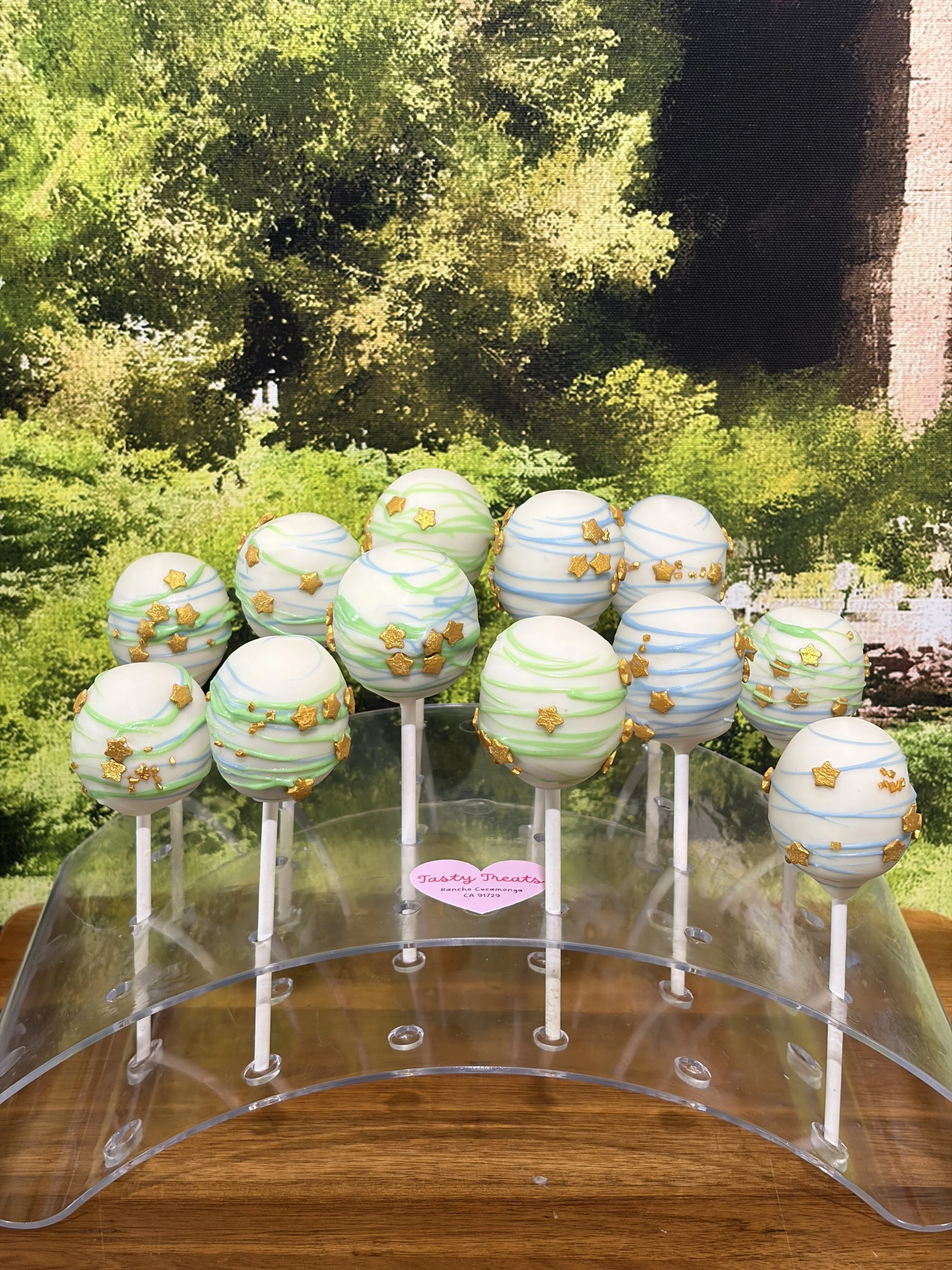 Green and blue marbled cake pops decorated with gold star sprinkles on a display stand