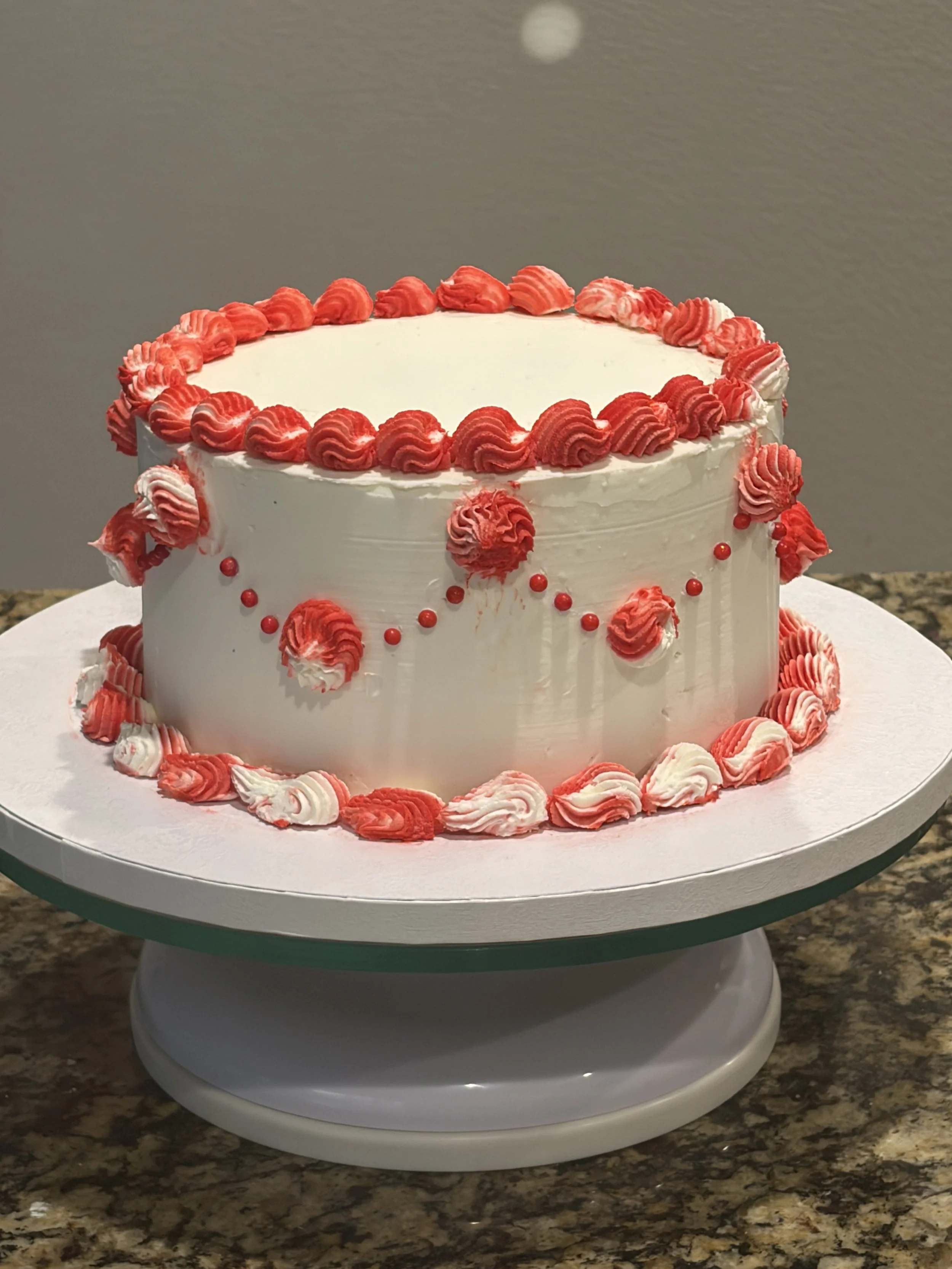 A white cake with red rose piping decorations on a white cake stand.