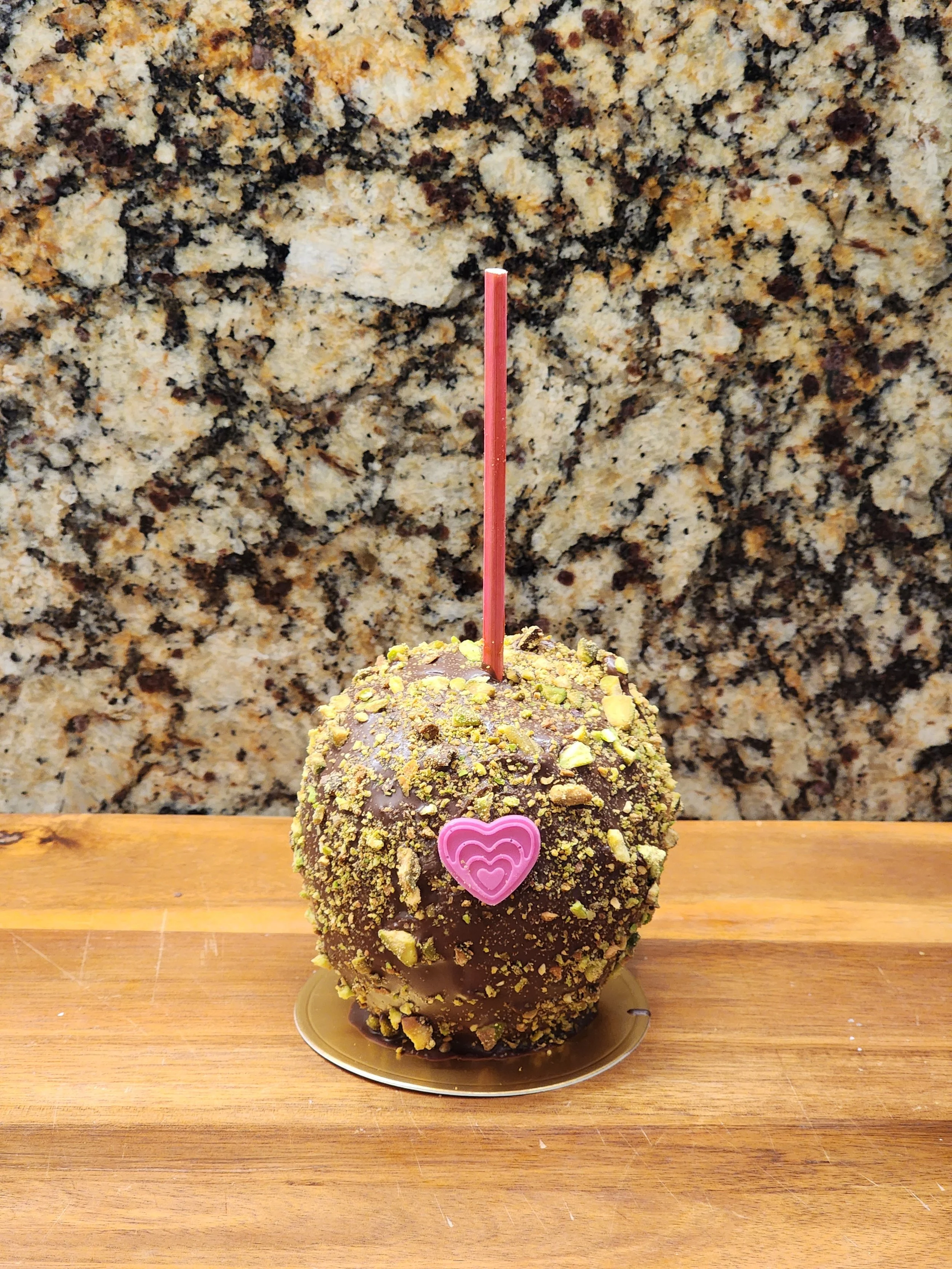 A caramel apple covered in gold glitter sanding sugar with a pink heart candy.