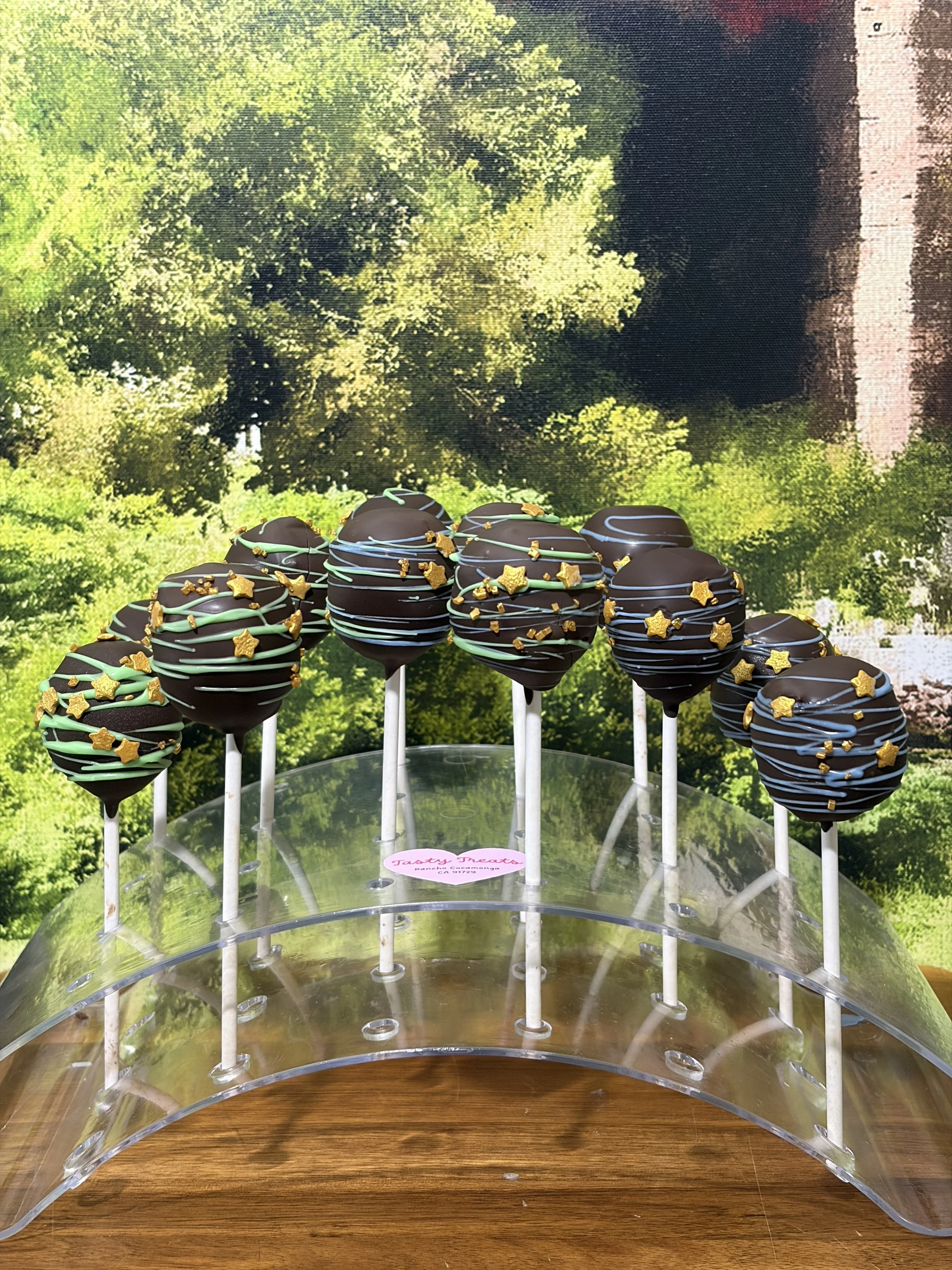 Dark chocolate cake pops decorated with gold star sprinkles on a display stand