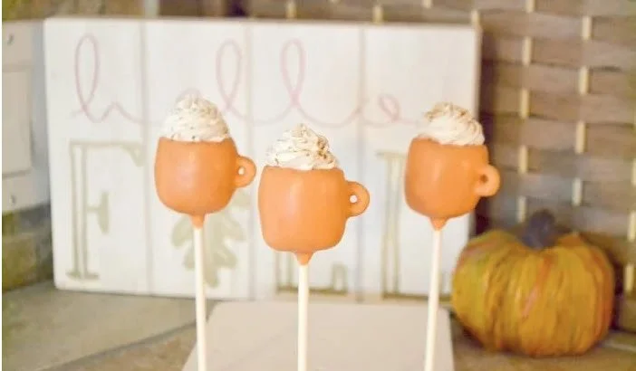 Cake pops shaped like mugs, dipped in caramel-colored chocolate and topped with a swirl of whipped cream, part of the Spiced Chai dessert lineup.