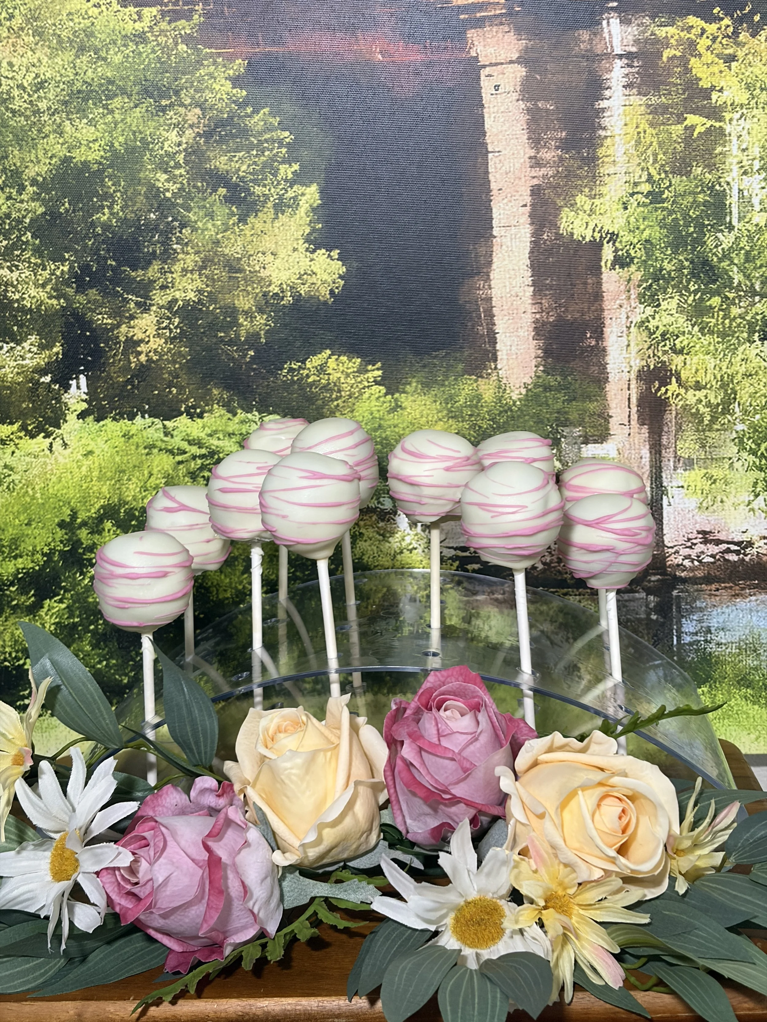 Pink and white swirl cake pops on a stand, garnished with fresh roses